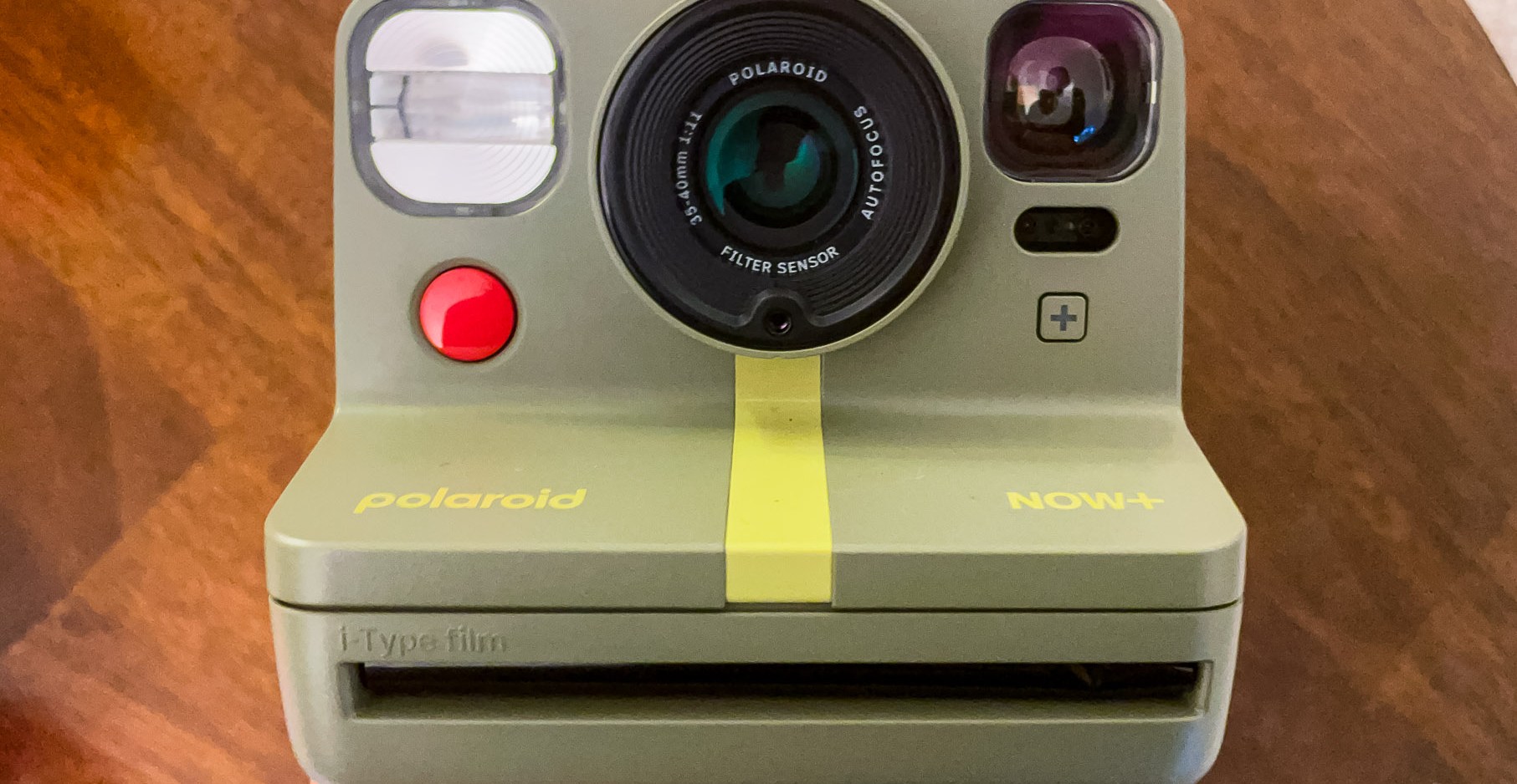 A closeup of a green second-gen Polaroid Now Plus held up against a brown background.
