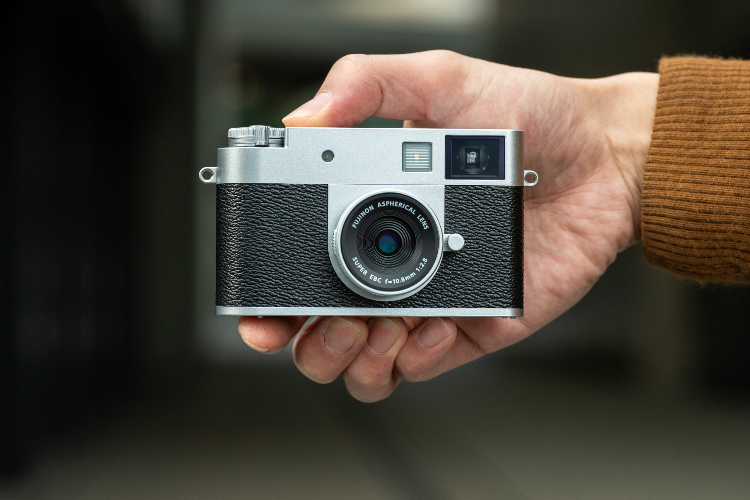 A silver and black Fujifilm X Half camera in a person’s hand.