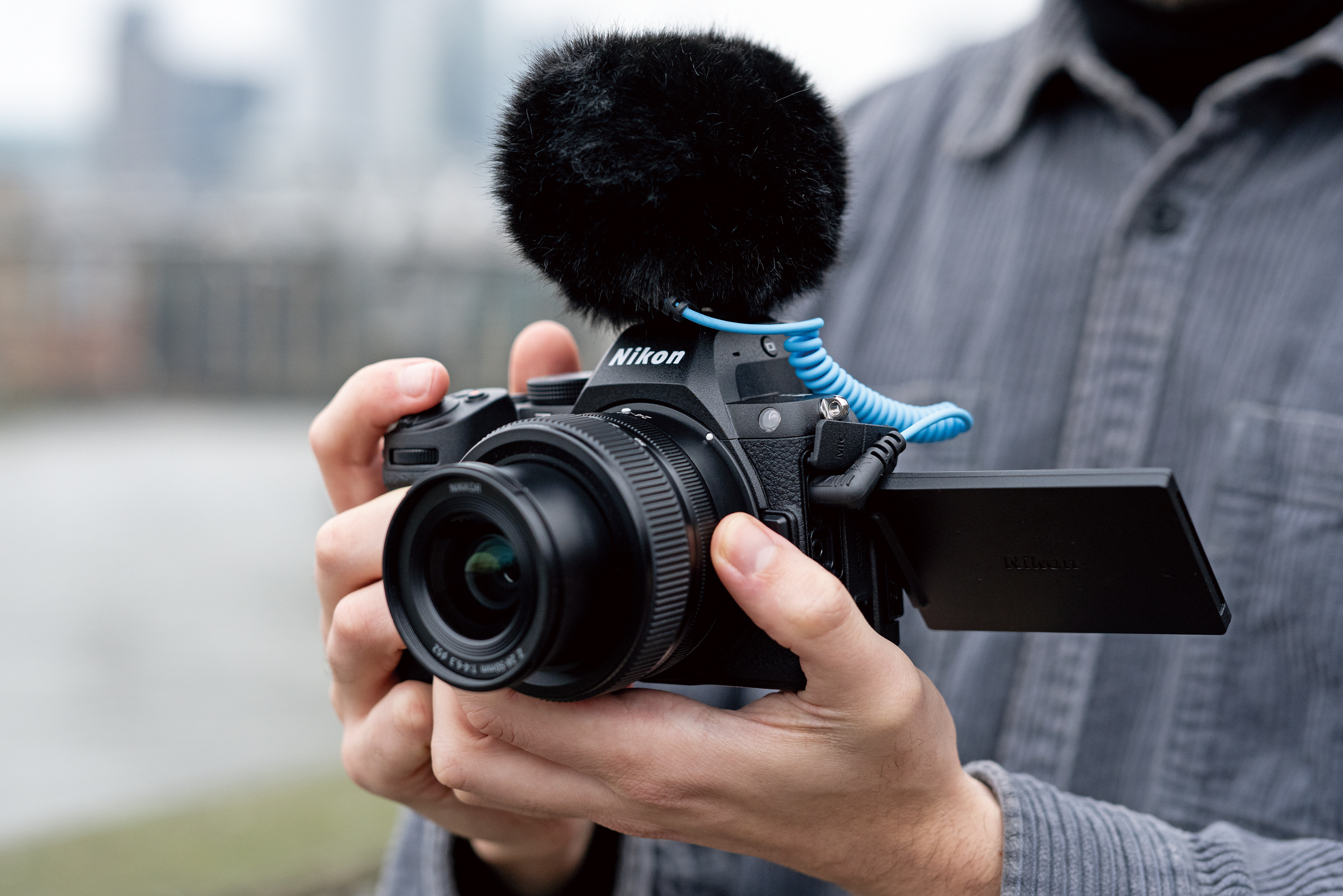 A person holding the Nikon Z5 II with its screen flipped out and a microphone attached.