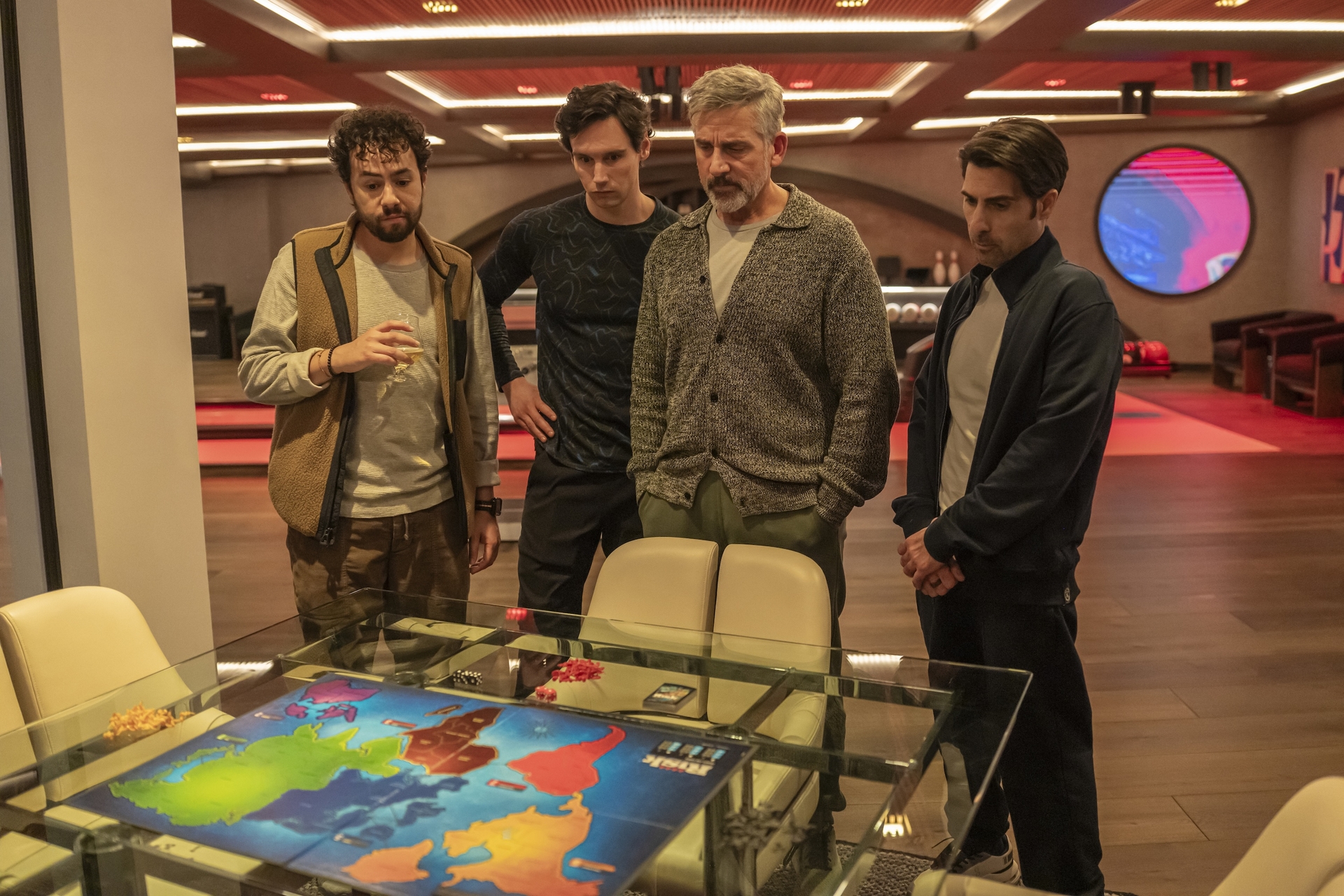 Four men standing together shoulder to shoulder while looking down at a Risk game board.