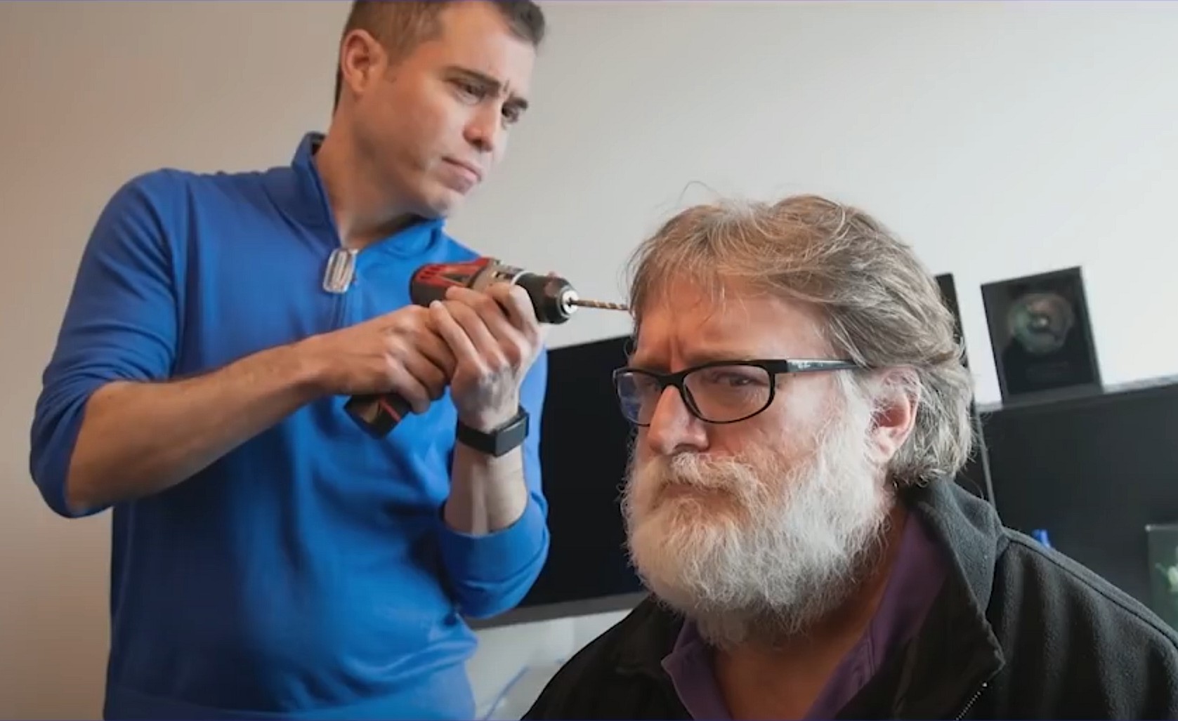 A man pretending to drill into Gabe Newell’s head.