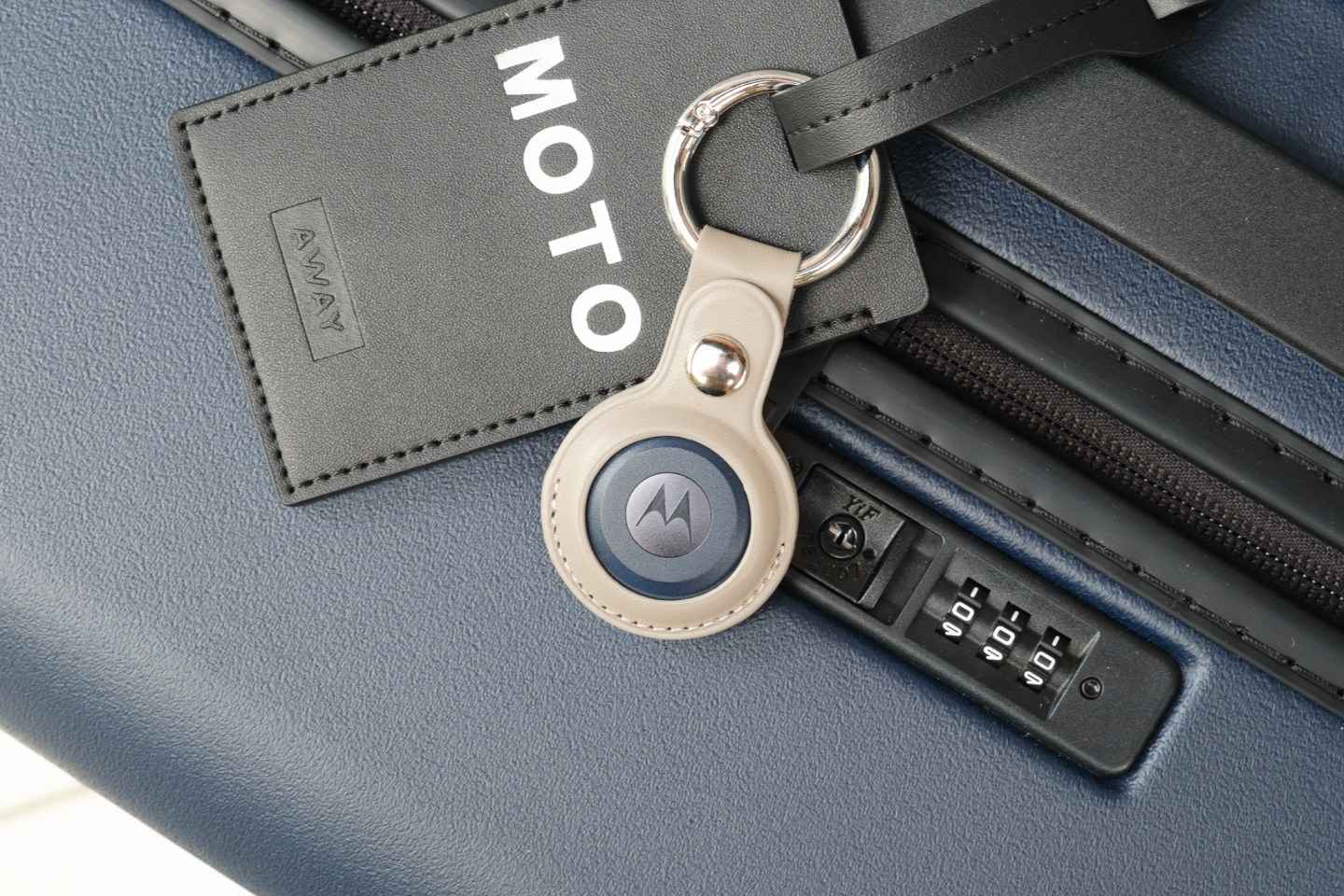A Moto Tag shown in a tag holder attached to a suitcase.