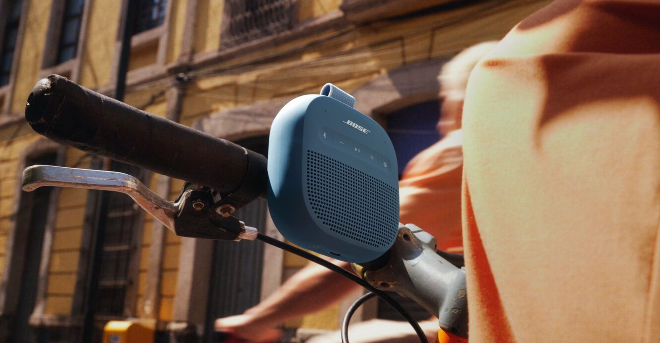 The Bose SoundLink Micro (2nd Gen) Bluetooth speaker strapped to the handle of a bicycle.