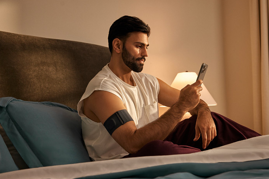 A person sitting in bed holding a smartphone with Garmin’s Index Sleep Monitor attached to their right arm.