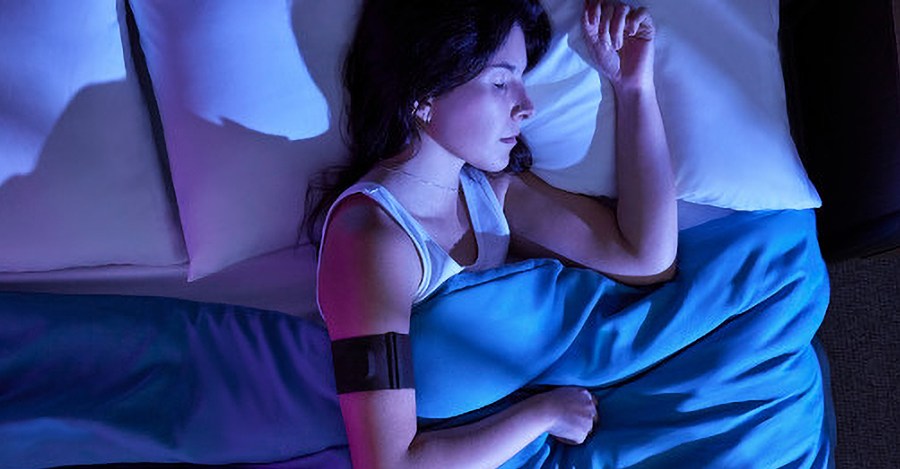 A person sleeping in bed wearing Garmin’s Index Sleep Monitor on their right arm.