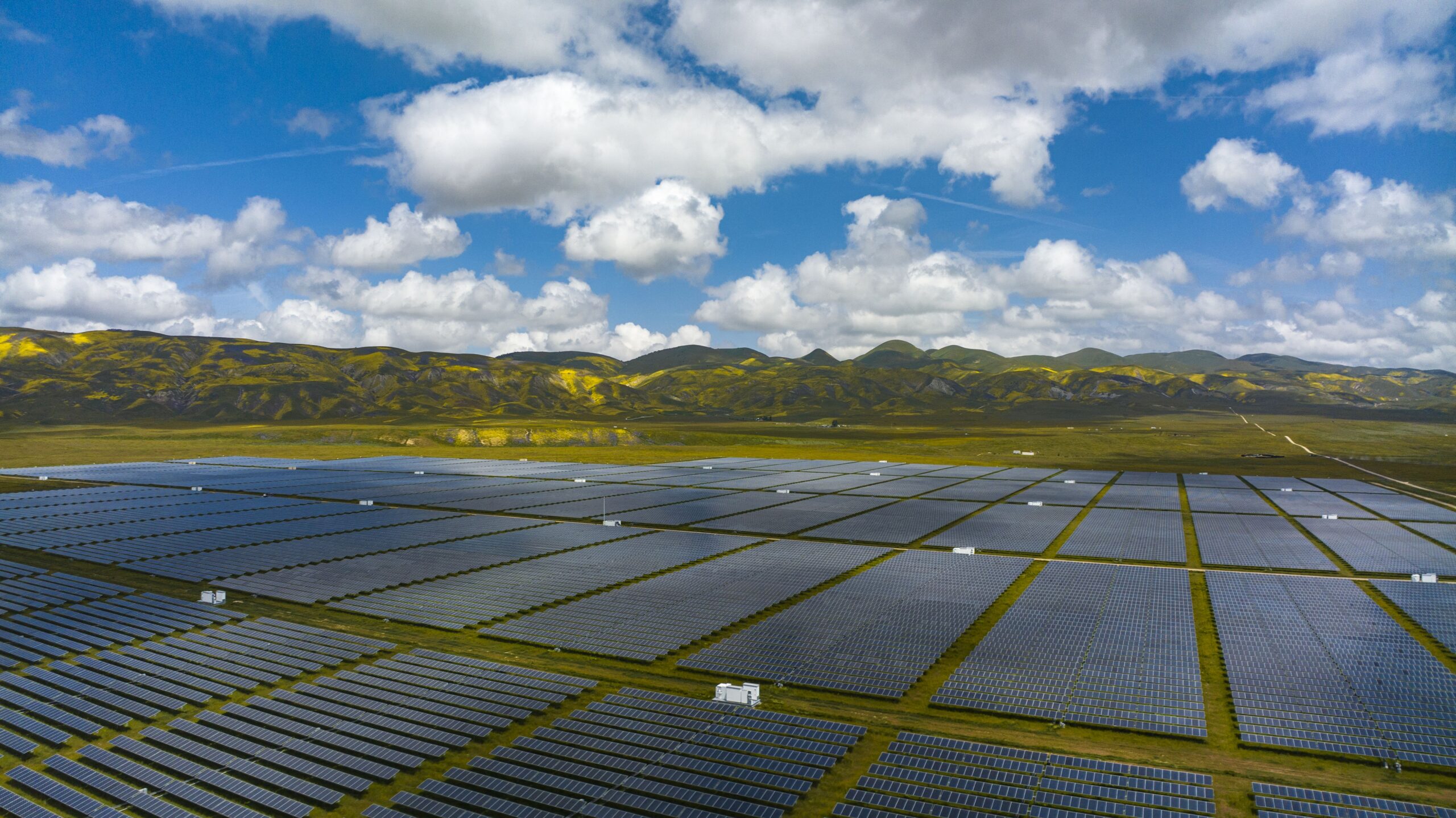 An aerial view of a vast spread of solar panels under a blue sky and clouds.