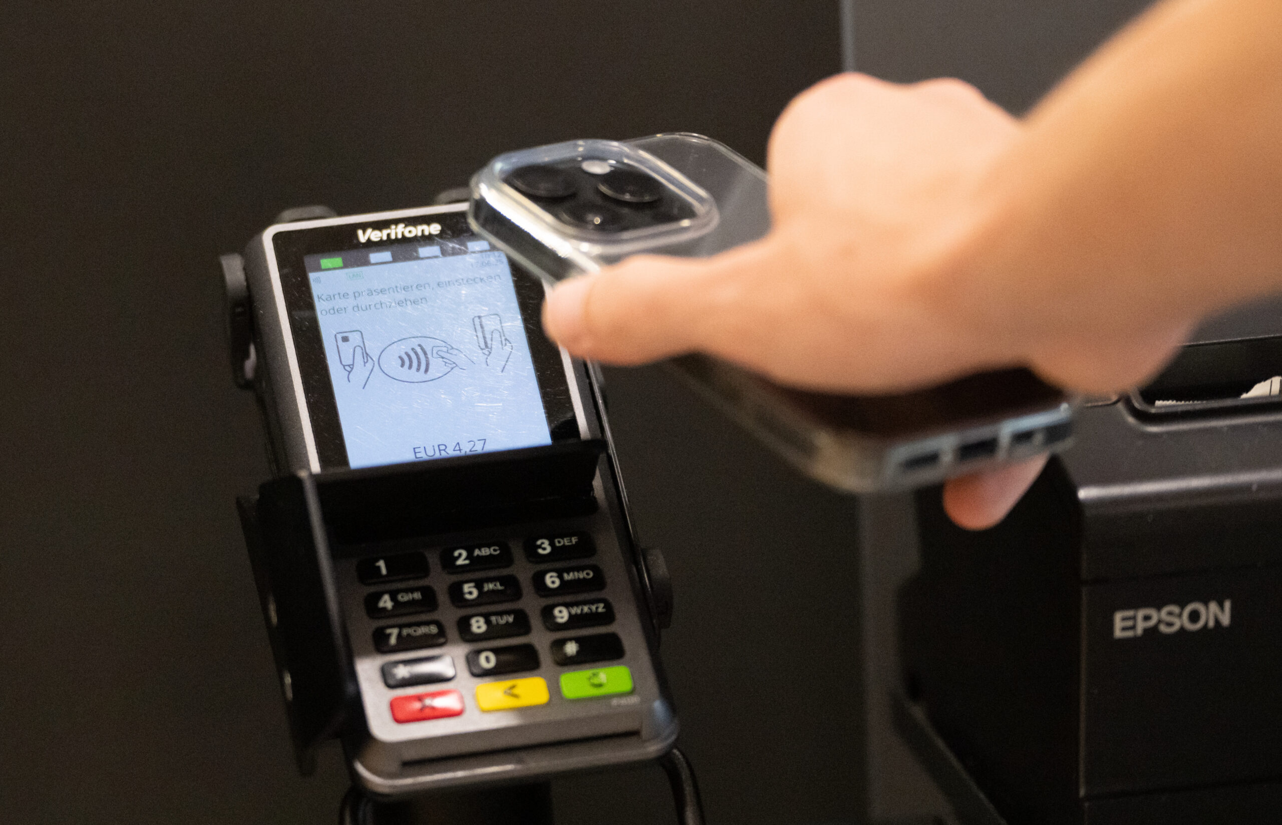 A person holds their cell phone up to a card reader at a self-service checkout.