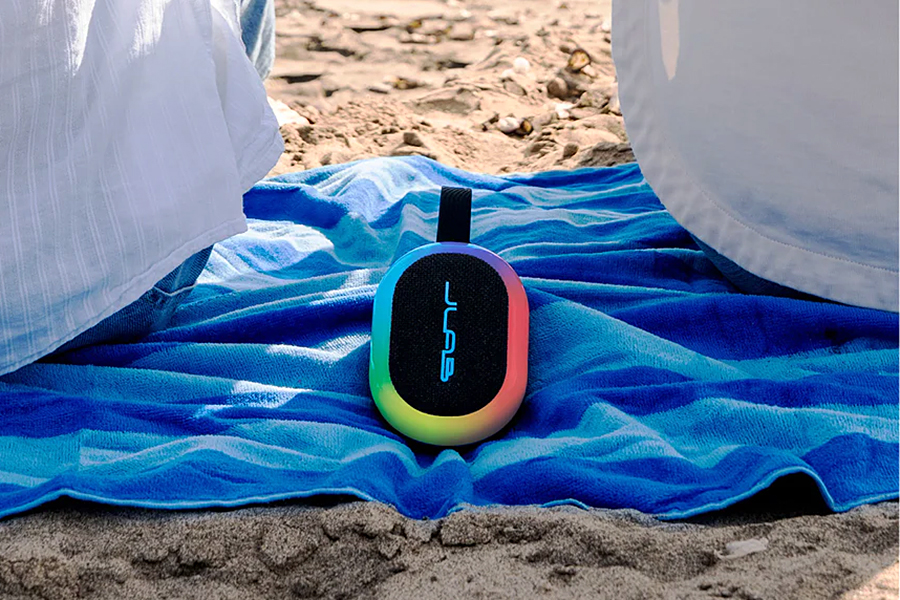 A JLab Bluetooth speaker on a blanket on a beach.