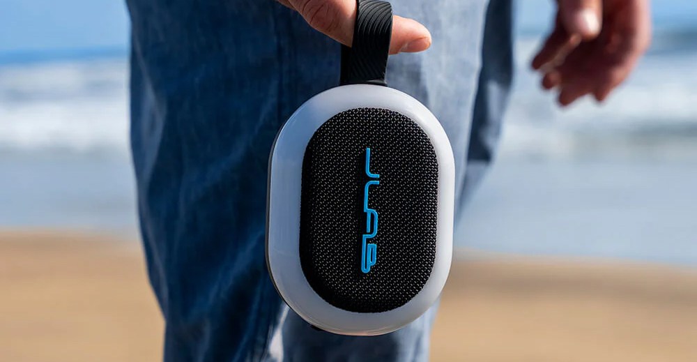A JLab Bluetooth speaker being held in someone’s finger using its carrying strap.