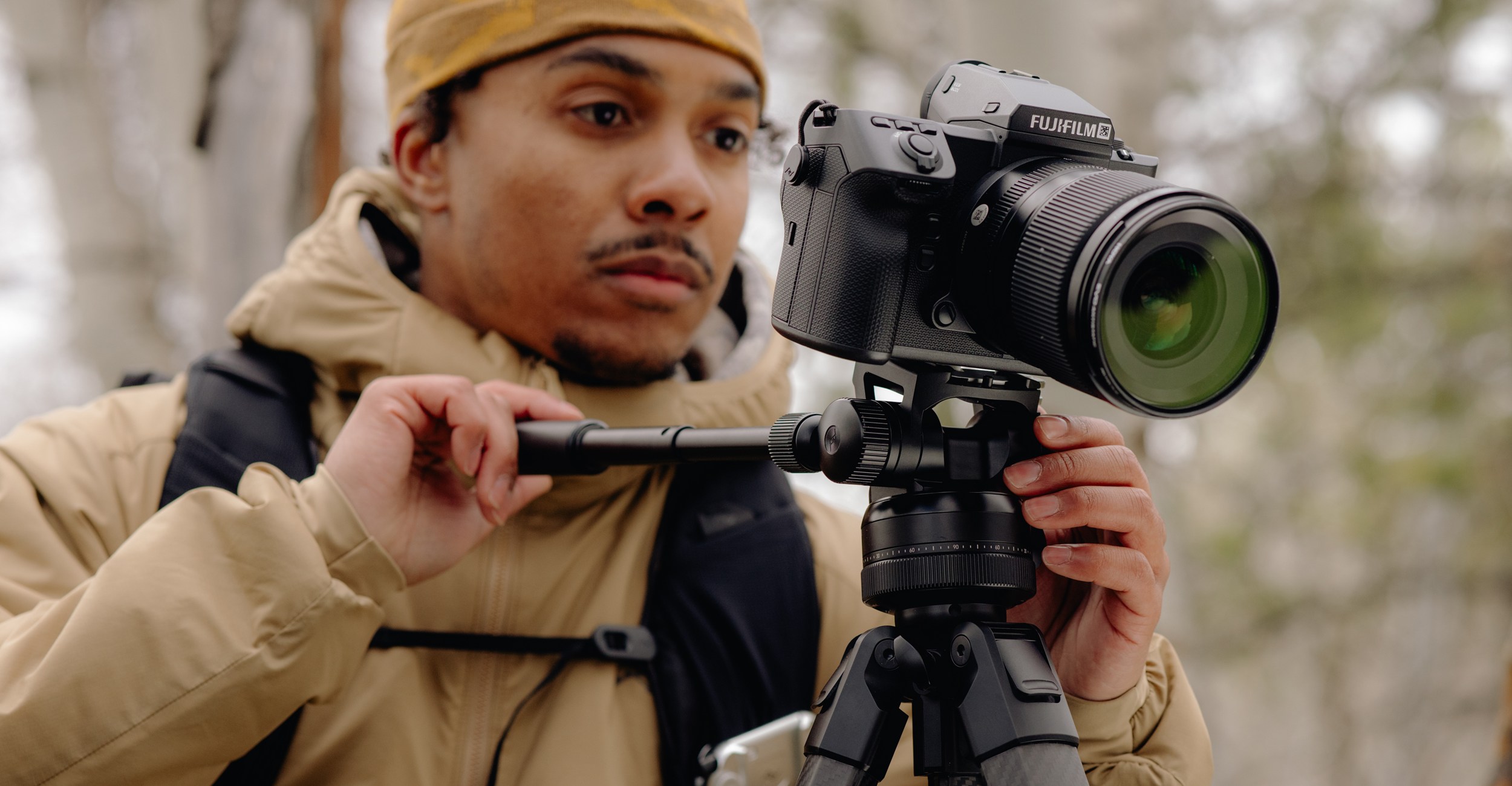 A photographer in a parka adjusts the angle of a Fujifilm camera attached to a Peak Design tripod.