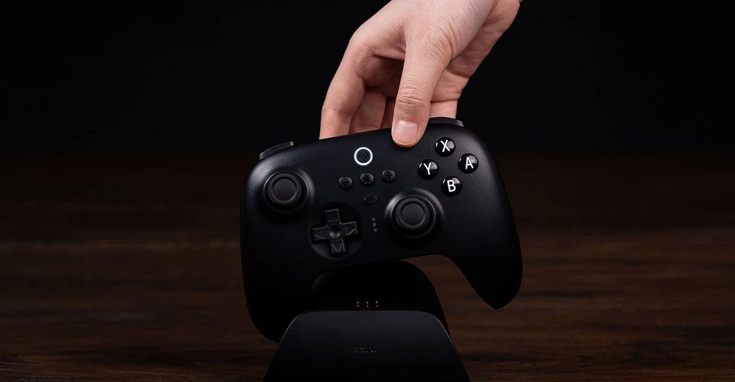 A hand putting an 8BitDo controller into its charging doc.