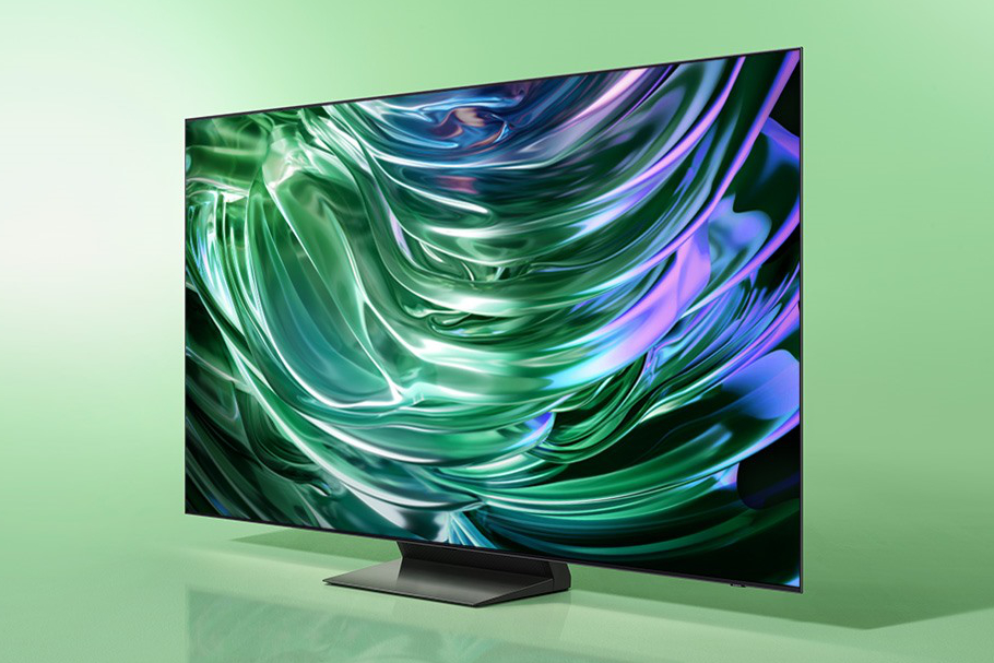 An image of the Samsung S90D OLED TV on a green gradient background. The screen is displaying abstract shapes glimmering.