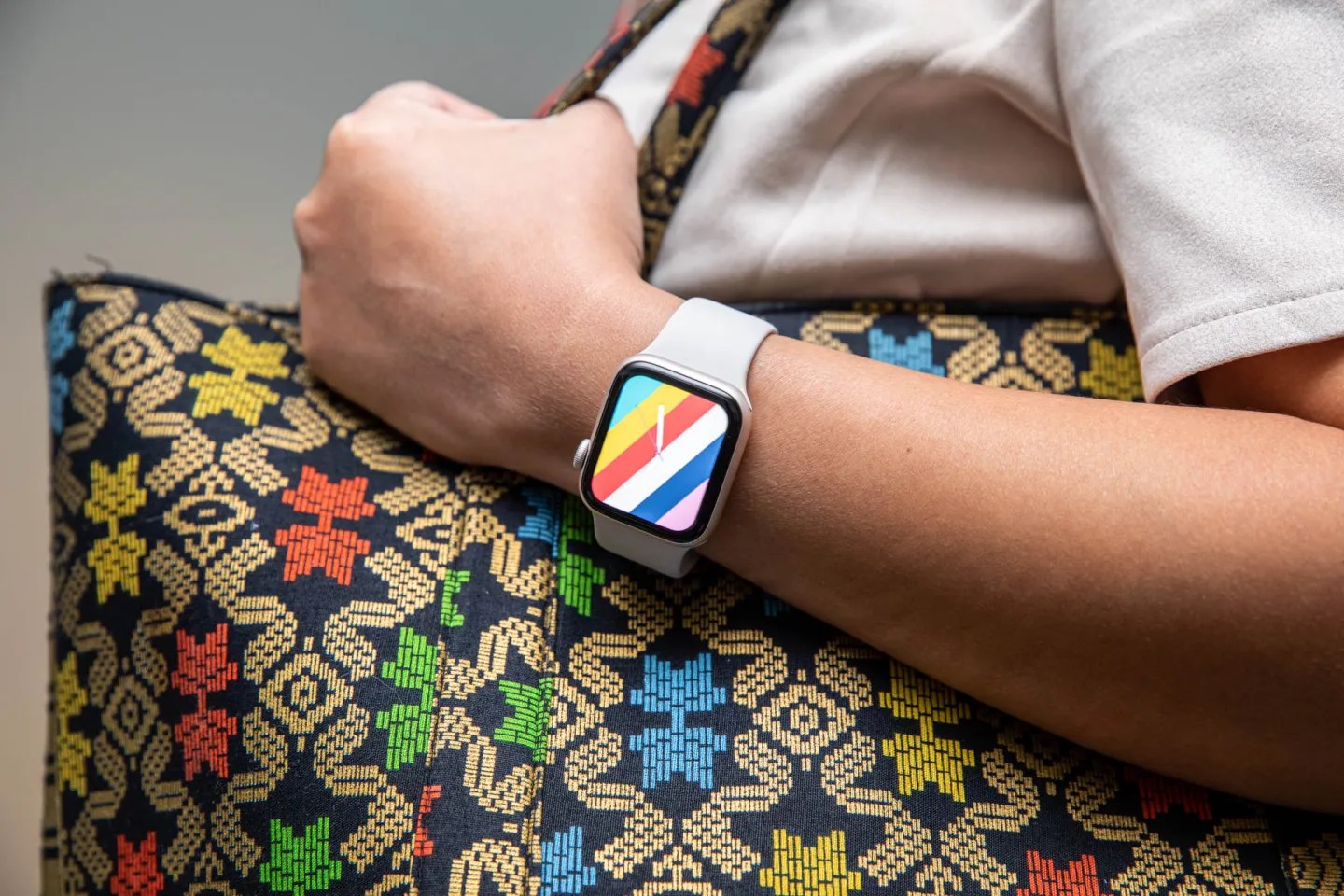 An image of a person wearing an Apple Watch SE 2022 with a colorful homescreen wallpaper. They’re carrying an equally eccentric bag.
