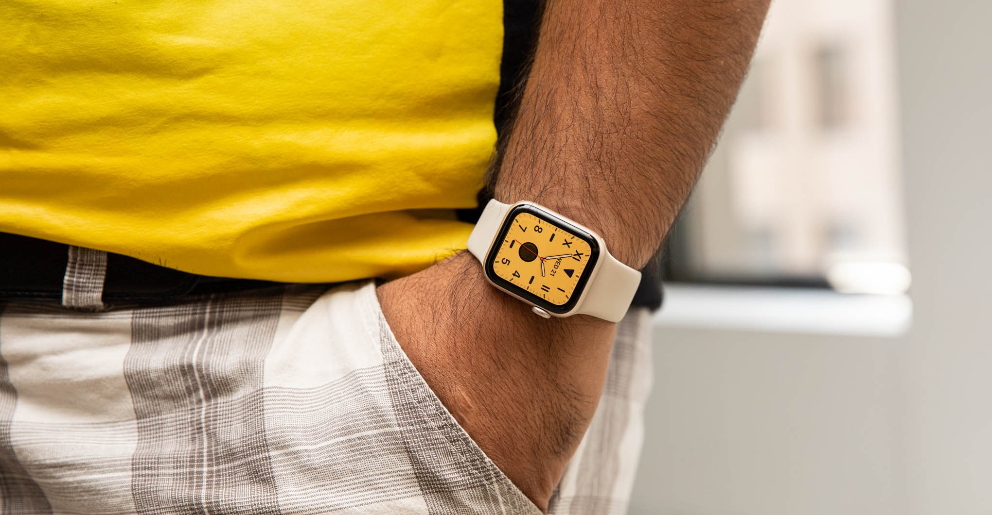 Man in yellow shirt with hand in pocket wearing second gen Apple Watch SE with a yellow watchface