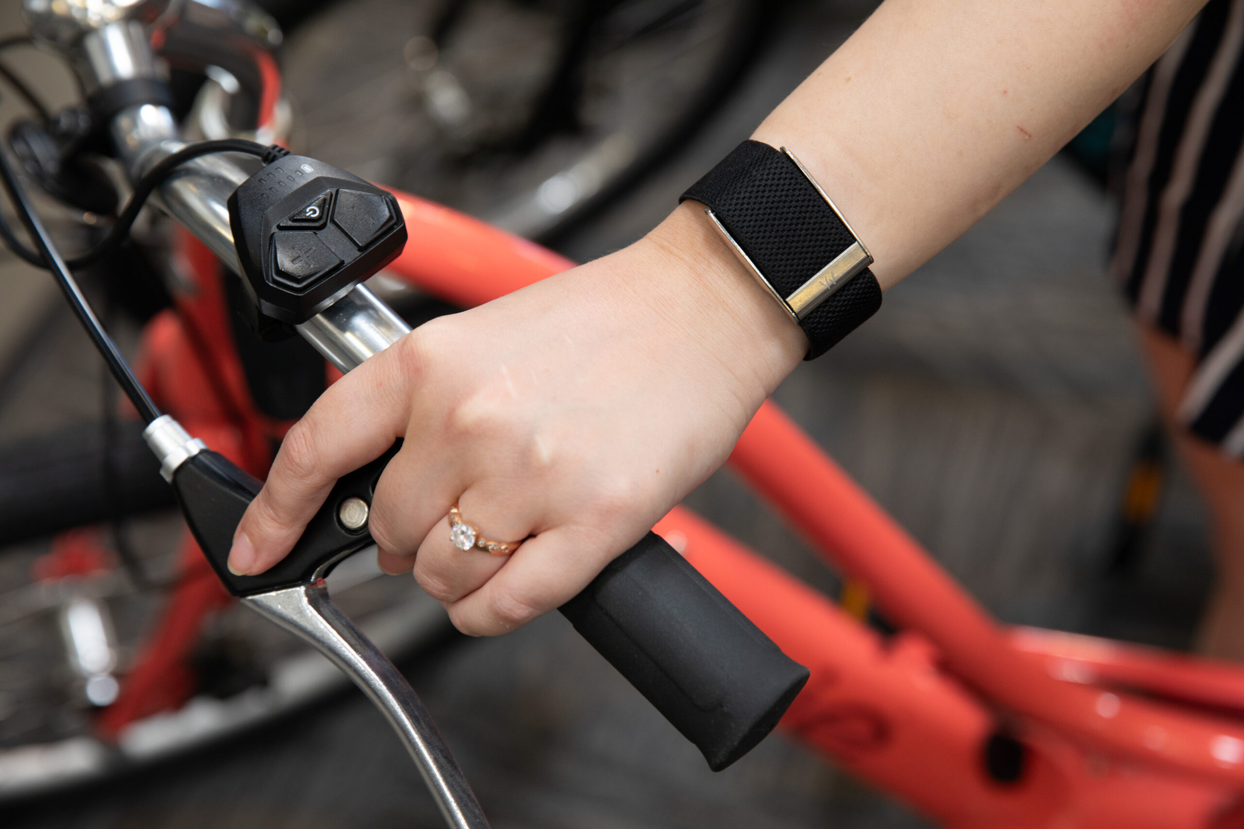 Overhead closeup of Senior reviewer Victoria Song’s wrist while wearing a black Whoop MG while holding the handlebars of a bright coral bike.