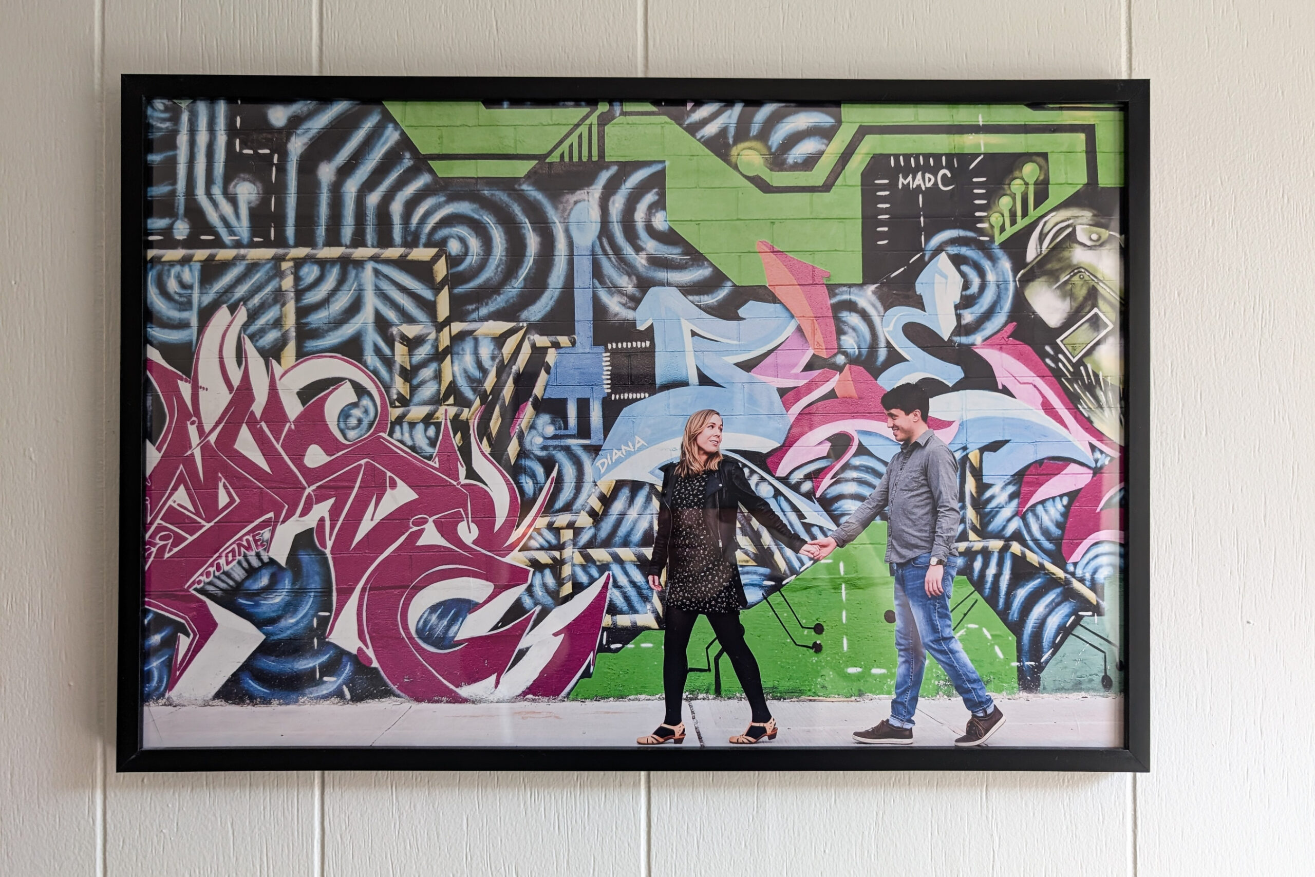 A poster showing a graffiti’d wall with two people in front of it walking hand in hand.