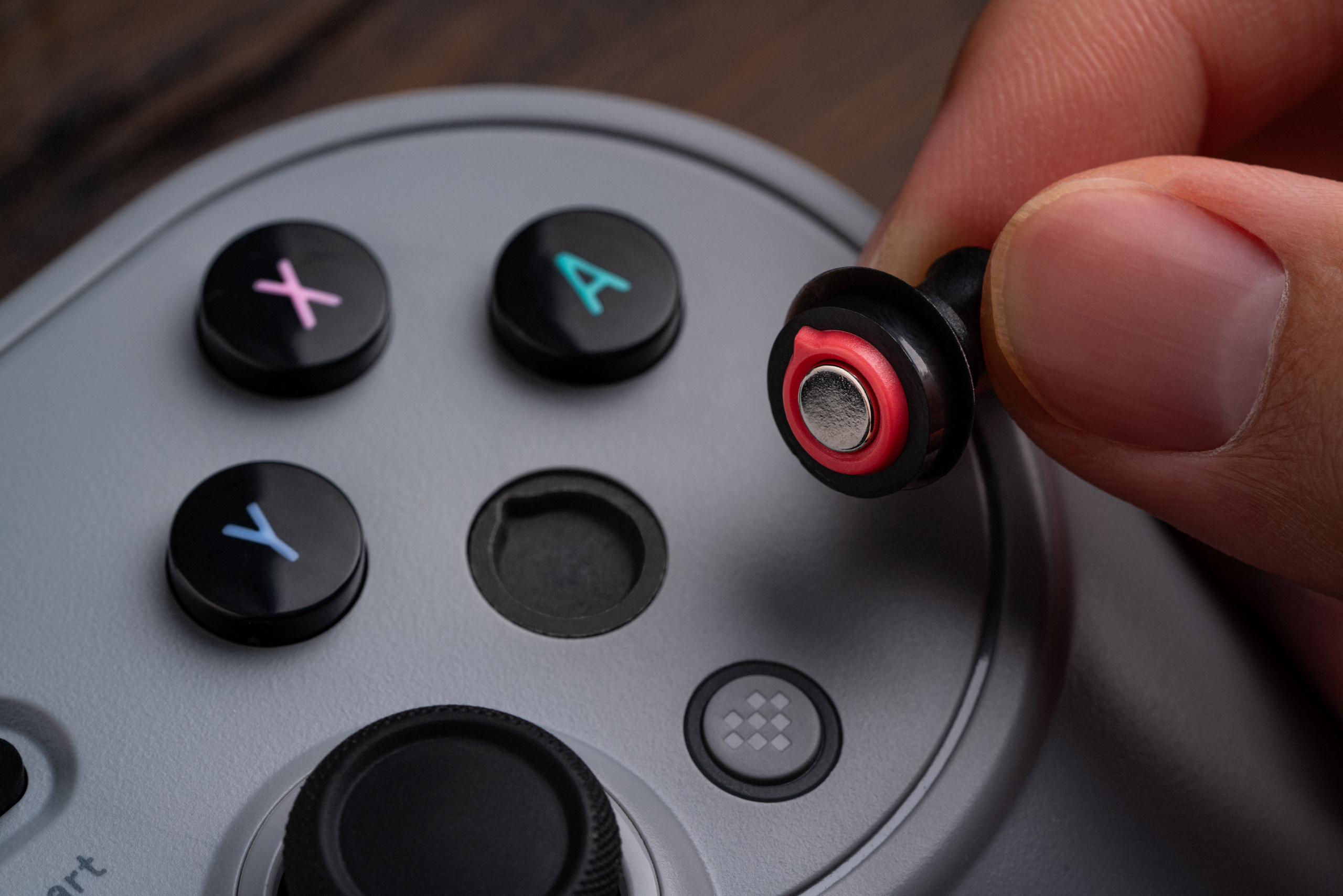 A person uses a small tool to remove a button from the face of the 8BitDo Pro 3 wireless controller.