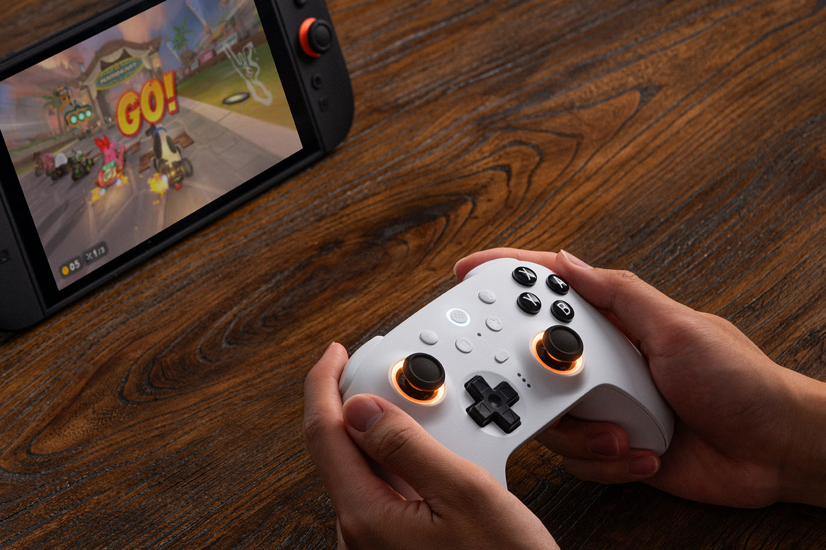 An image showing someone holding a white 8Bitdo Ultimate 2 Switch 2 Bluetooth controller. It’s powered on and controlling a session of Mario Kart World.