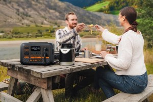 The Bluetti AC2P Portable Power Station on a picnic table with two people enjoying a meal.