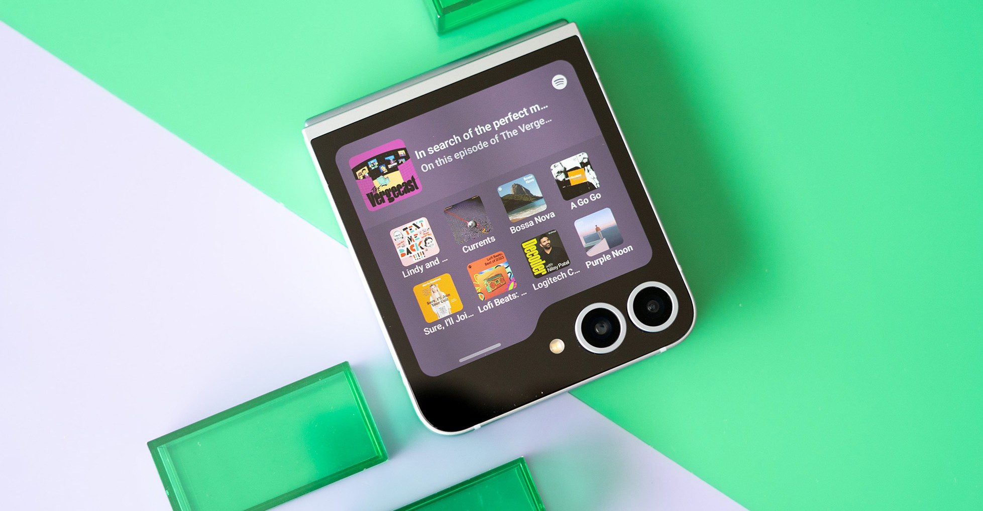 Photo of Samsung Galaxy Z Flip 6 on green and purple background showing cover screen.