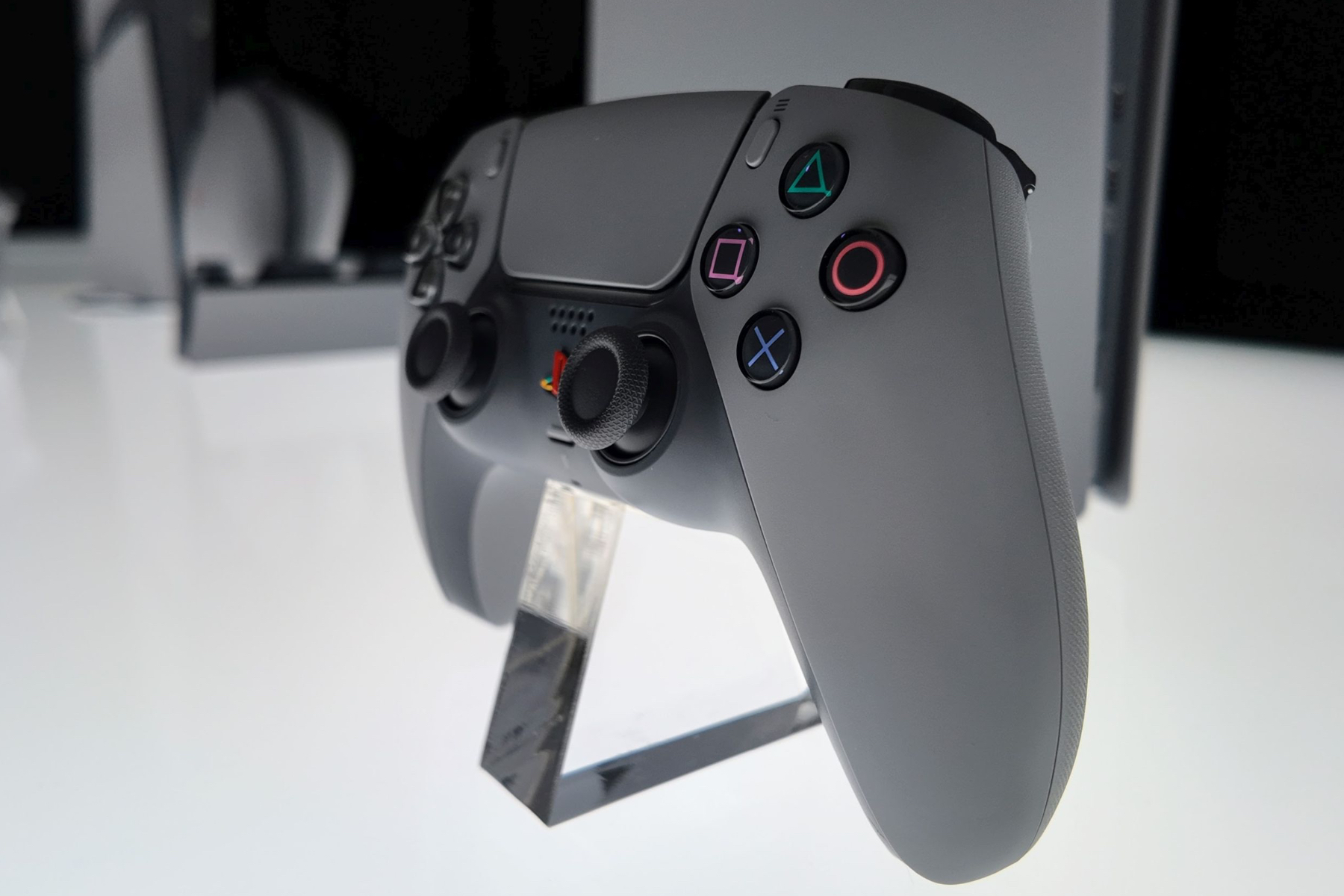 An image of the 30th Anniversary PlayStation 5 DualSense Controller resting on a stand on a white table.
