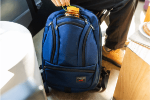 Blue backpack with somebody putting a water jug inside the middle pocket