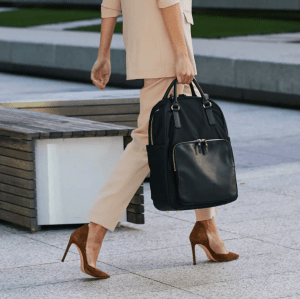 Woman walking down urban street holding backpack in one hand