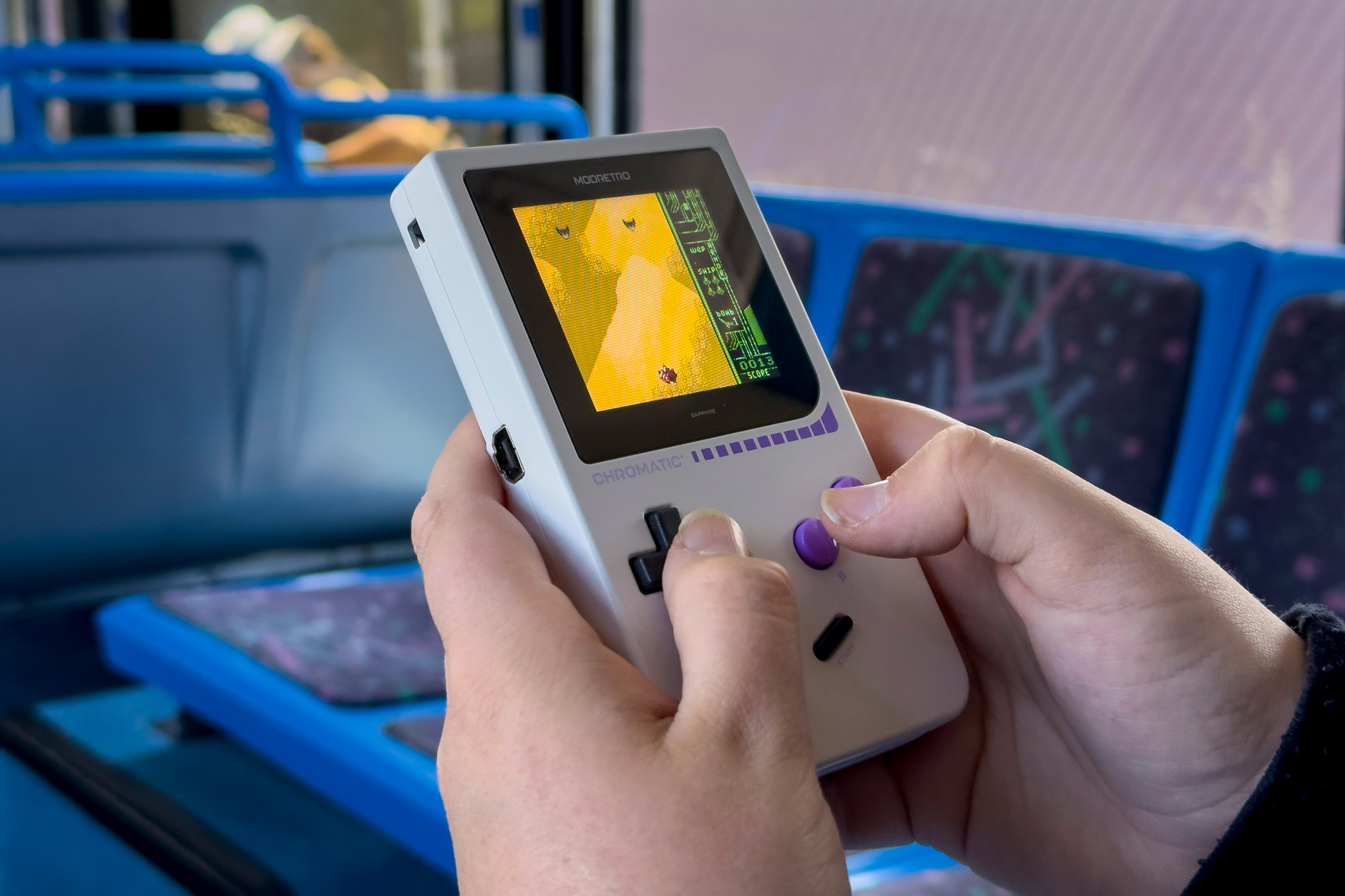 A closeup of a person playing the ModRetro Chromatic handheld while riding public transit.