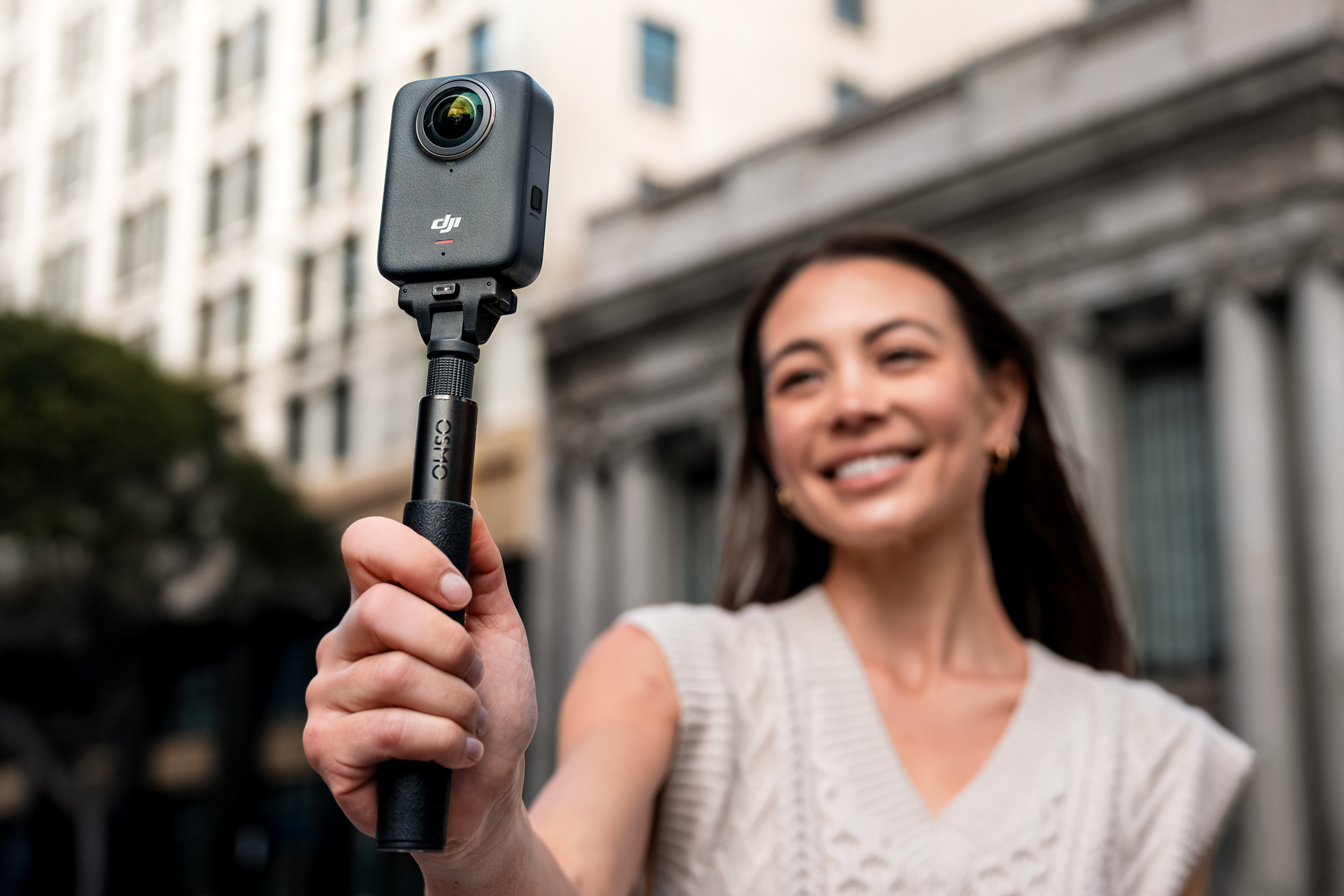 A person holds the DJI Osmo 360 action camera attached to a short selfie stick.
