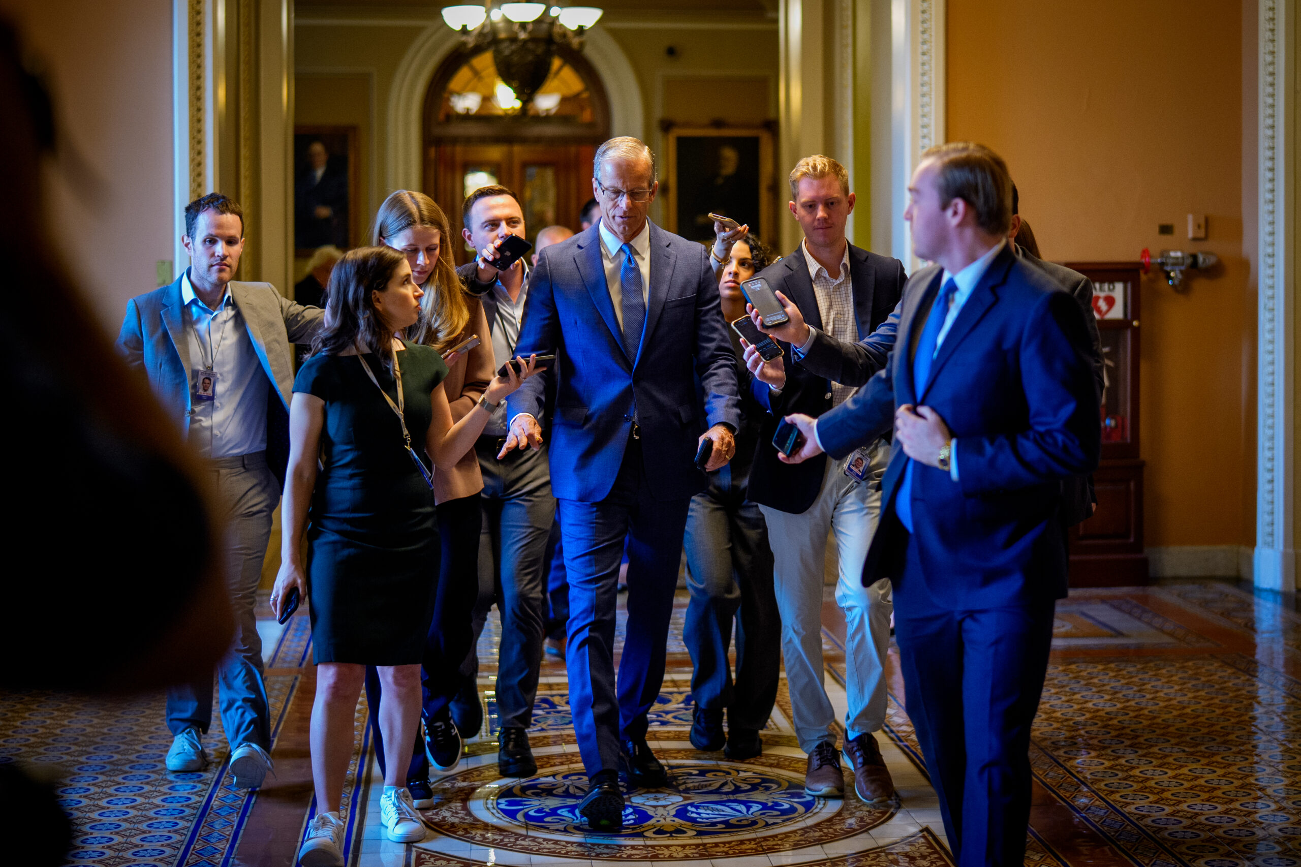 A group of people in suits walking down the hallway, including Senate Majority Leader John Thune.