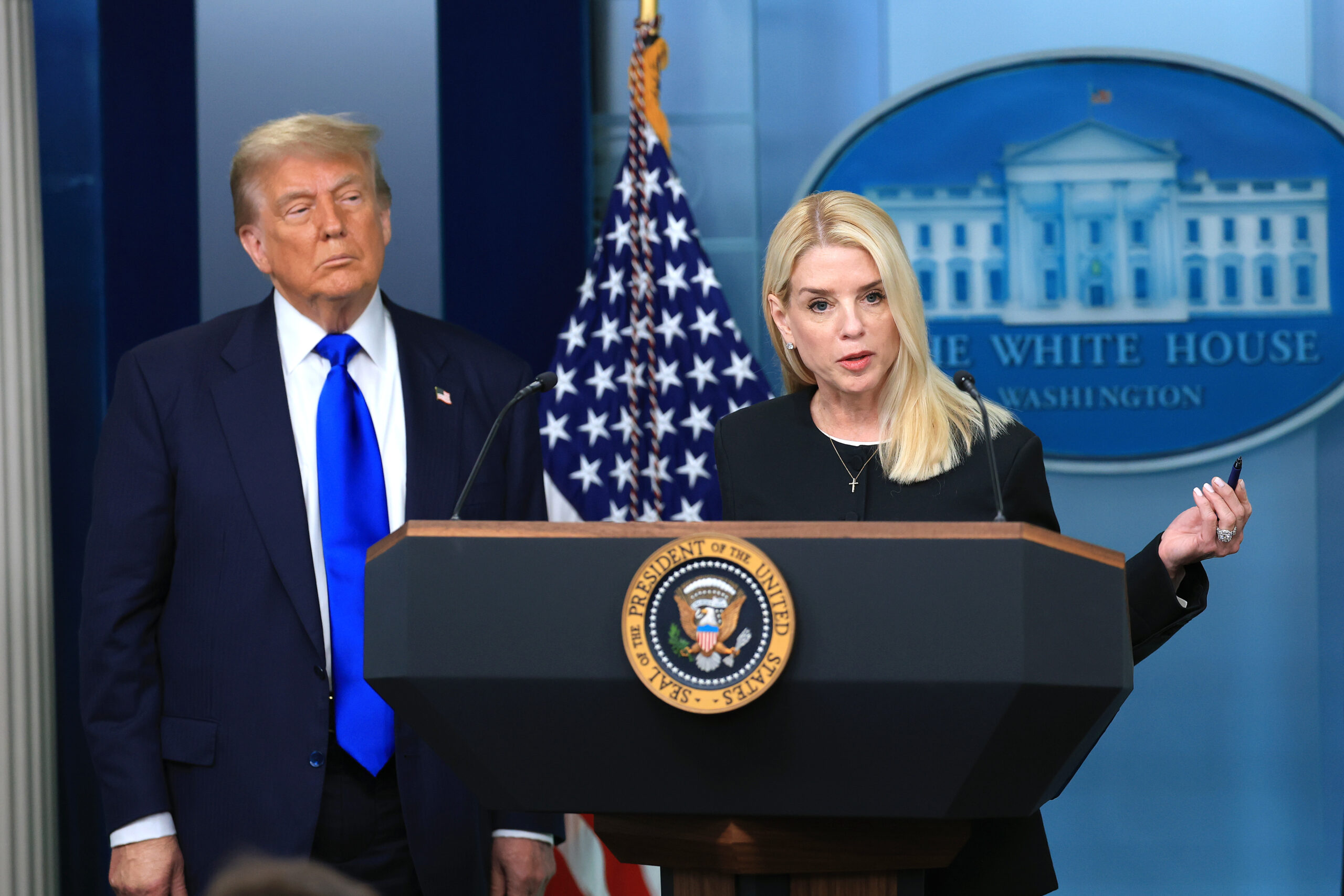 Attorney General Pam Bondi at a lectern alongside President Donald Trump