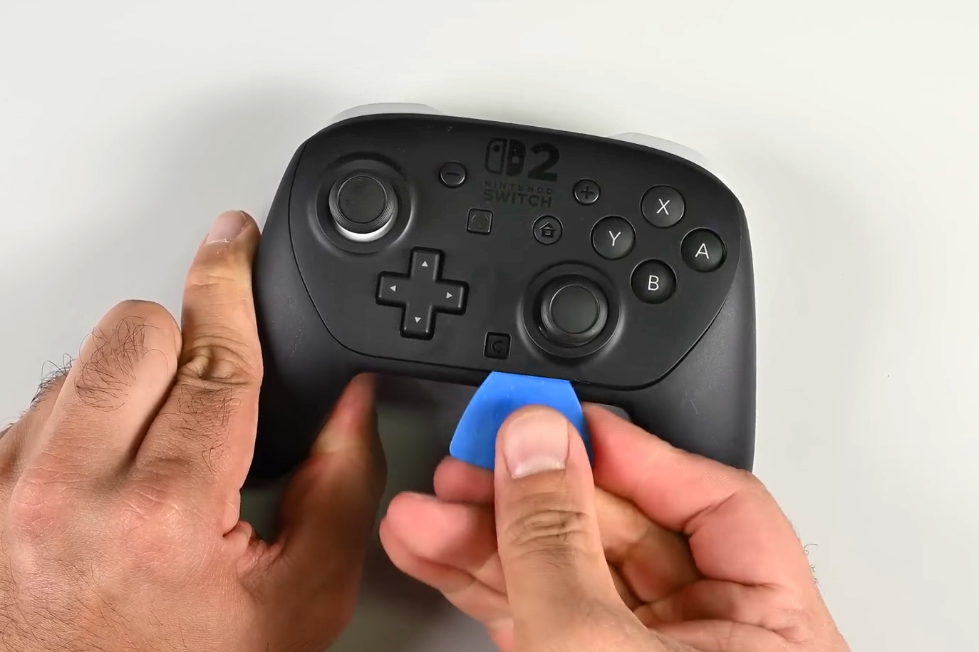 A blue prying tool is used to remove the Nintendo Switch 2 Pro controller’s faceplate.