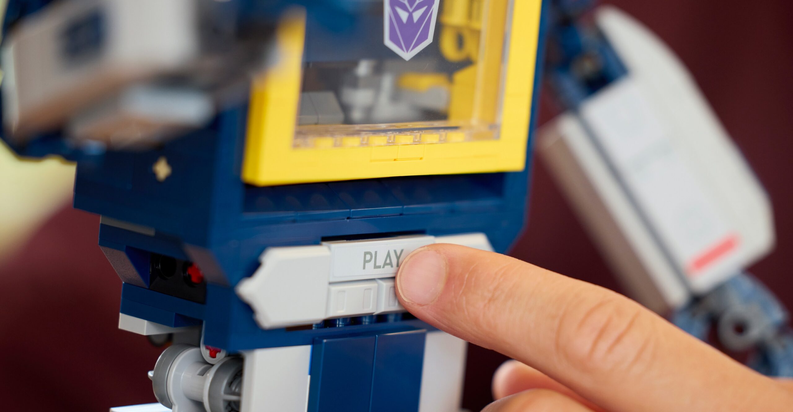 A person presses a play button on the Lego Transformers Soundwave model.
