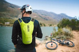 Biker rider wearing backpack with river and bike in background