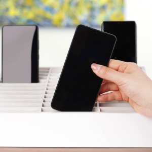 A hand putting a phone into a slotted phone holder with two phones already in.