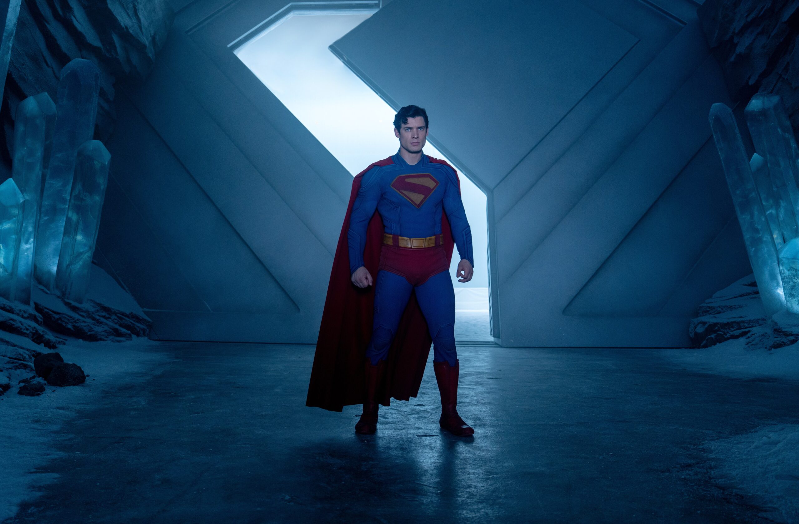 A man in a blue and red costume standing in a room that seems to be made of metal and crystals.
