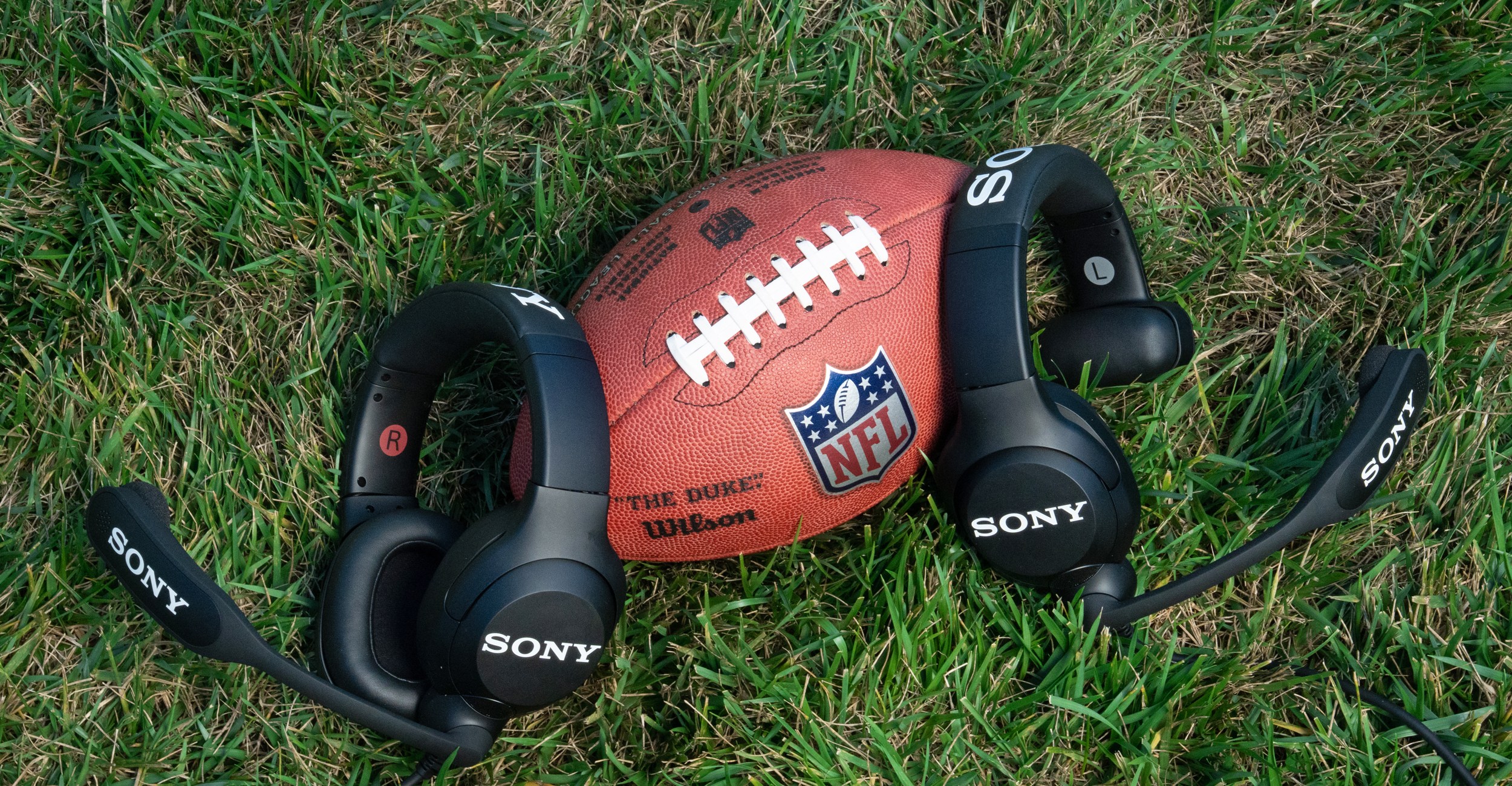 Two of Sony’s NFL Coach’s Headsets sitting next to a football on grass.