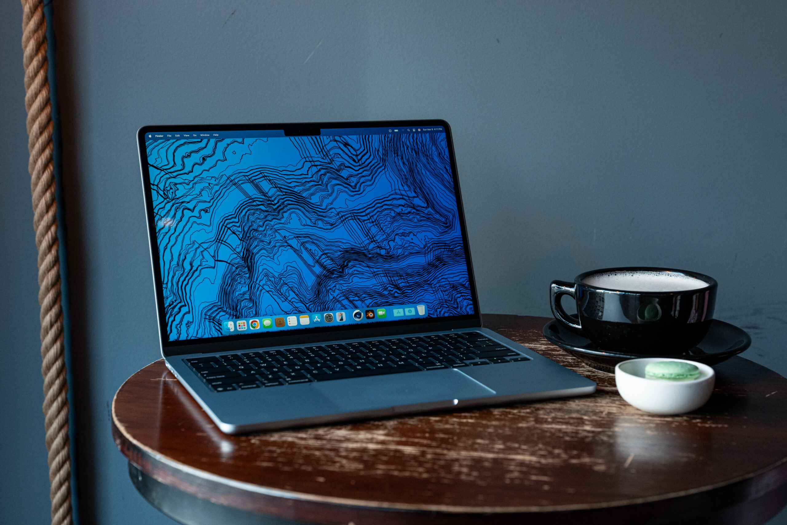 The M4 MacBook Air sitting on a table next to a cup of coffee and dish with a macaron. 