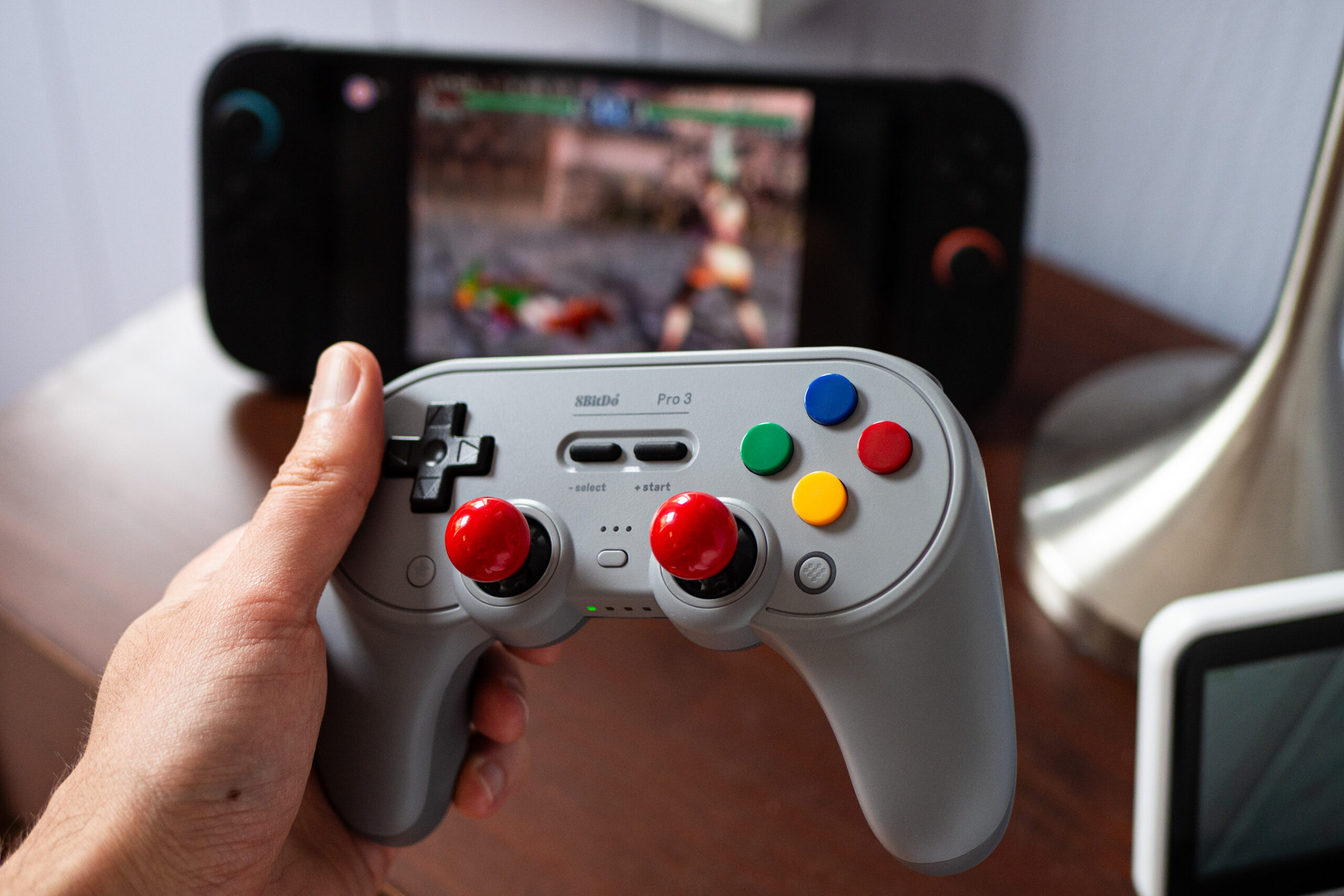 An image of a person holding the 8BitDo Pro 3 gaming controller, which is equipped with colorful analog sticks in place of grippy caps, as well as colorful face buttons instead of the standard ABXY array.