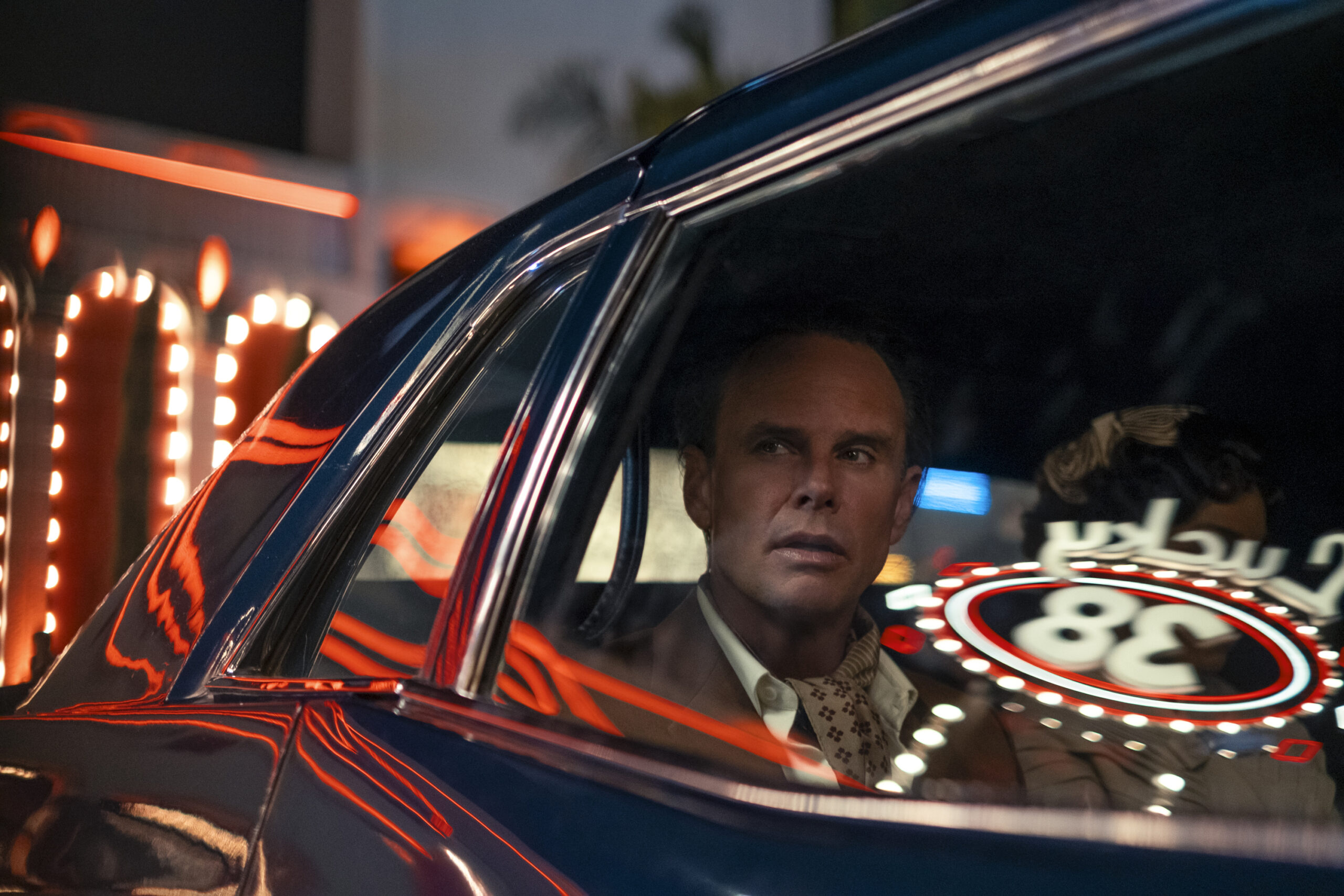 Production image from Fallout season 2 featuring Walton Goggins before he was transformed into the Ghoul in a car under the bright sign for the Lucky 38 casino.