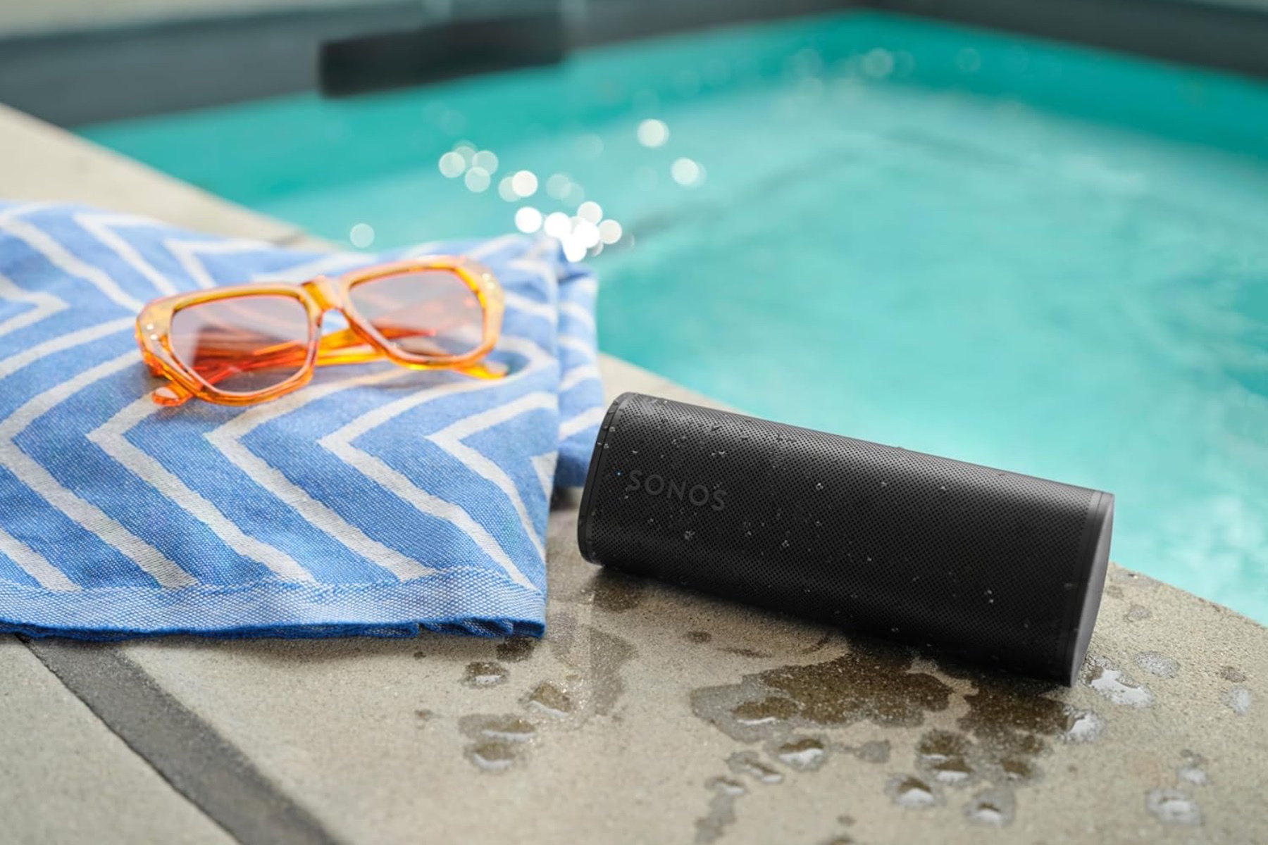 The Sonos Roam 2 next to a pool, blanket, and pair of sunglasses.