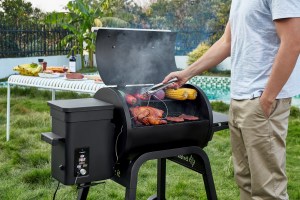 The Zelos 450 AI smart grill by Brisk It, being used outside to cook a variety of BBQ foods.