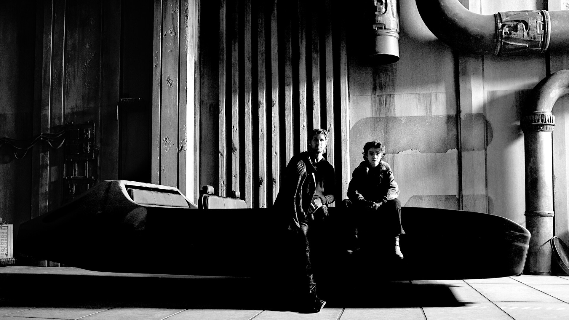 A black and white photo of Ryan Gosling and Flynn Gray on set for Star Wars: Starfighter. The pair are sitting on a floating vehicle in what appears to be a garage of some kind.