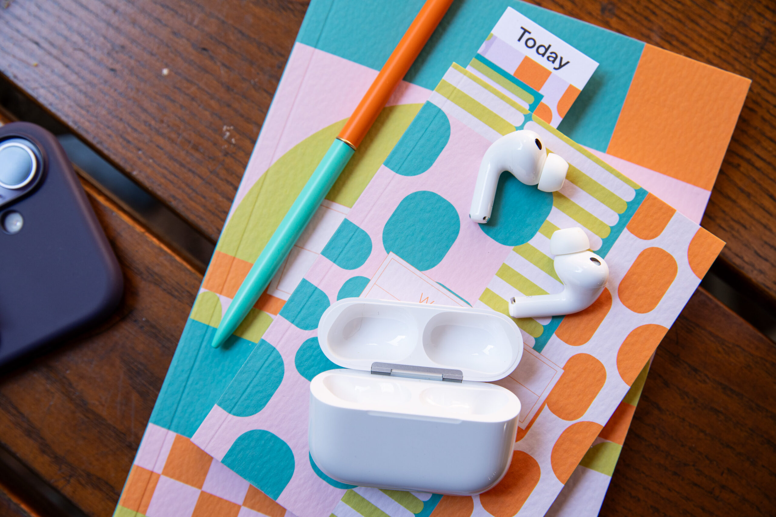 The AirPods Pro 3 outside of their case on a very colorful, patterend notebook. 