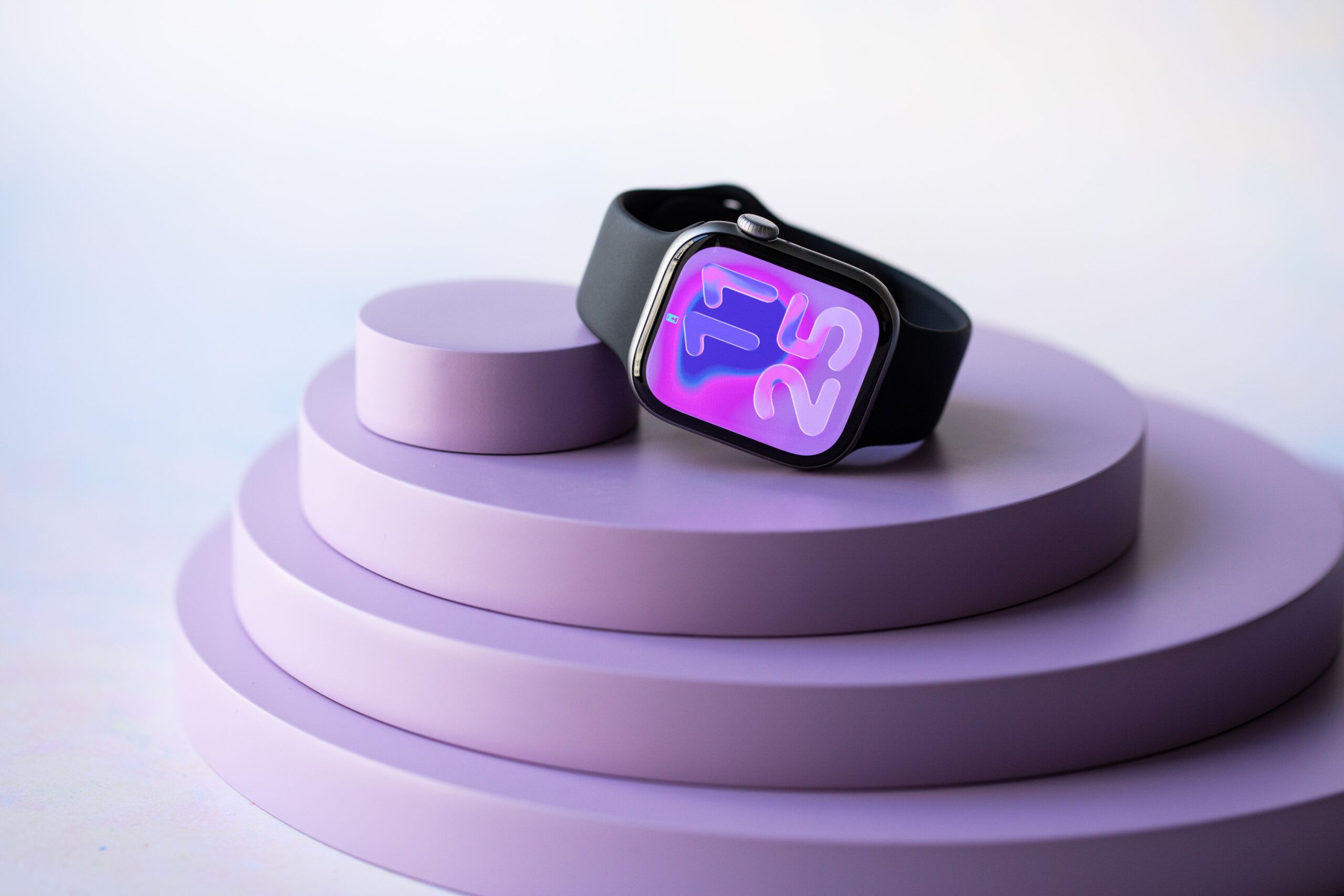 The space gray Apple Watch Series 11 sitting on an angle atop a series of concentric purple discs with the Flow watchface shown.