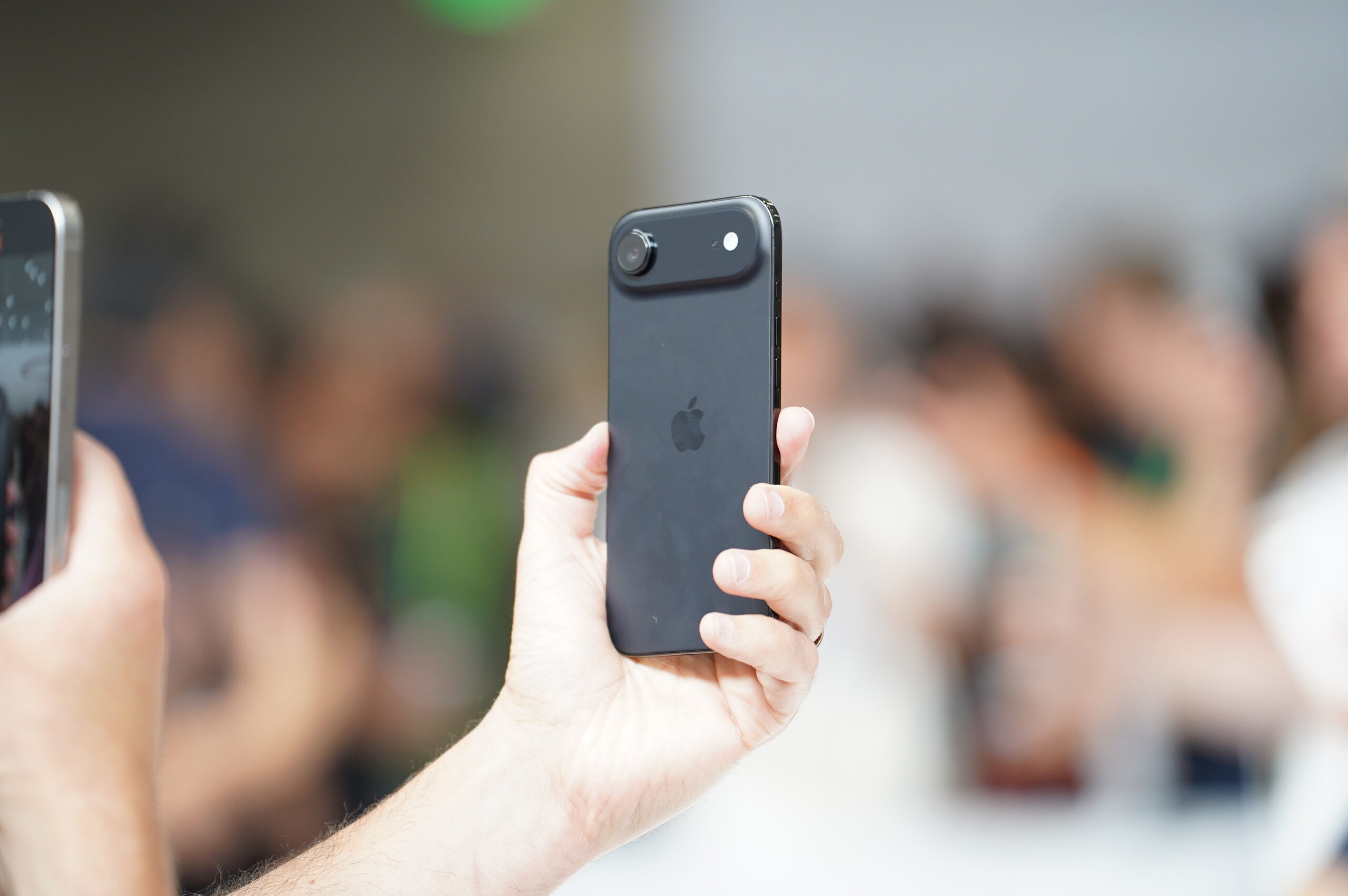 The iPhone Air being held by a hand in a crowded room.