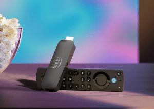 An Amazon Fire TV Stick 4K Max streaming stick with its remote sitting beside a bowl of popcorn in front of a TV.