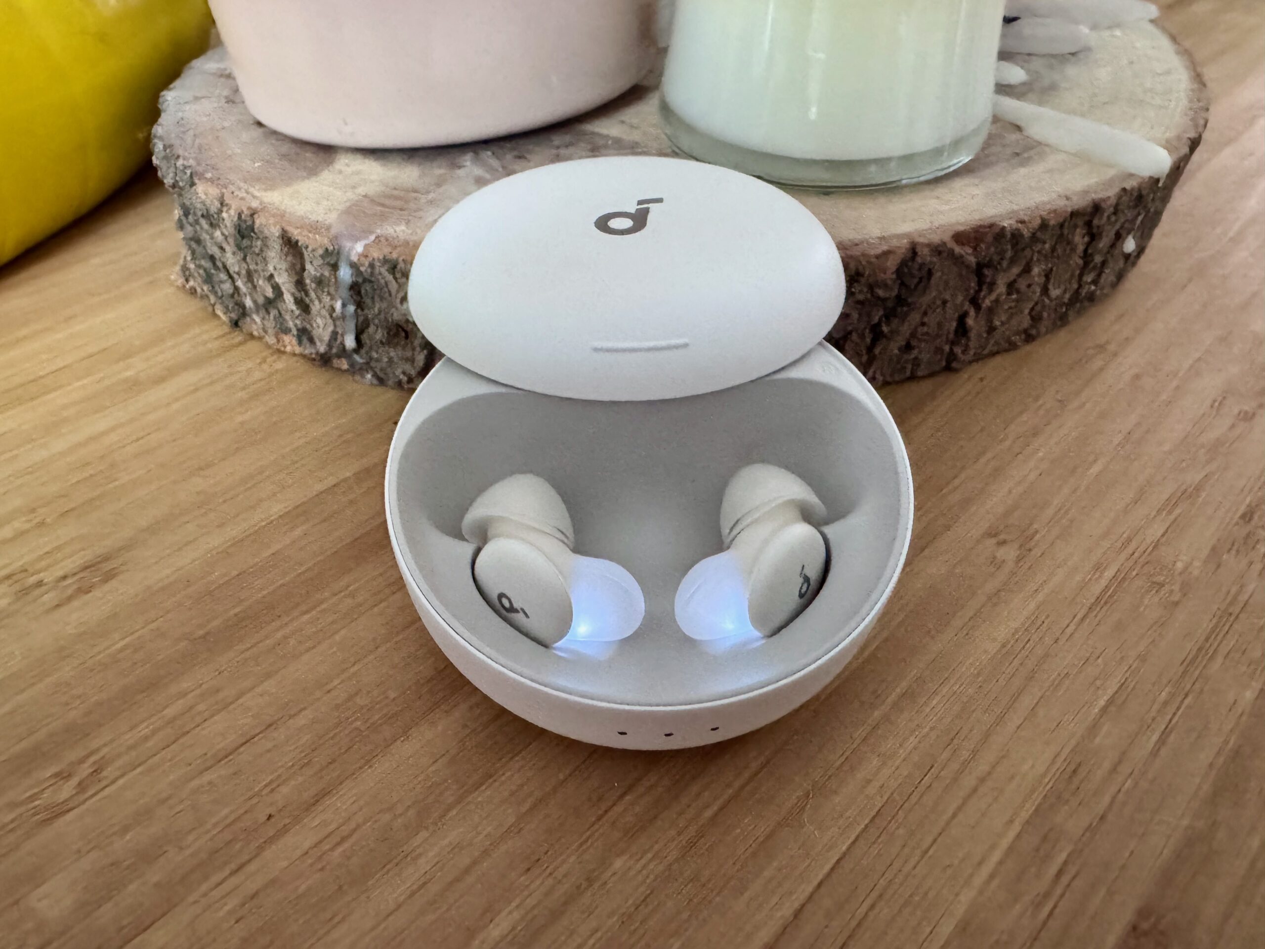 Anker’s Soundcore Sleep A30 earbuds in the charging case with the top slid open on a wooden surface. 