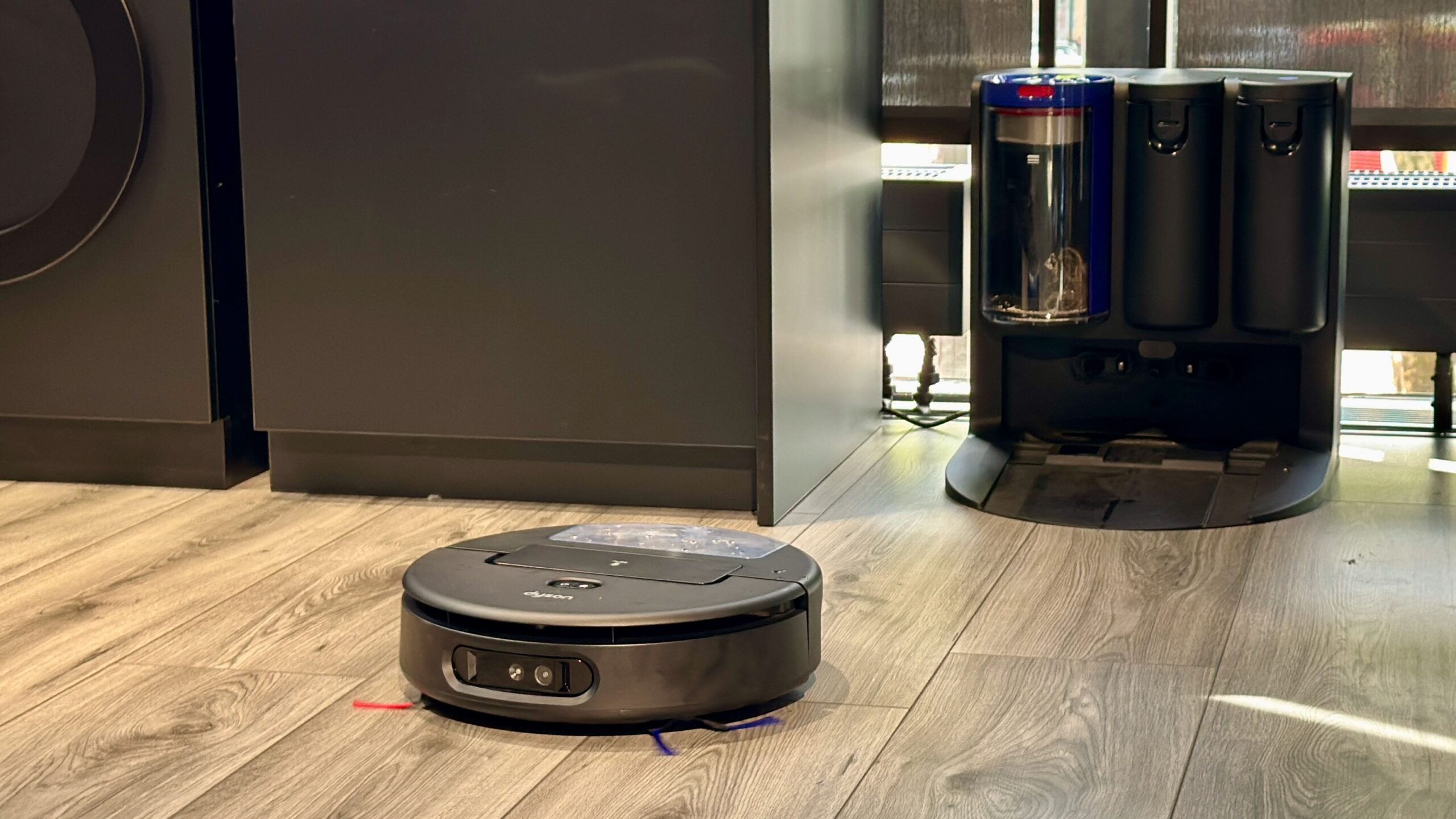 A robot vacuum on a hardwood floor in front of a large charging dock.