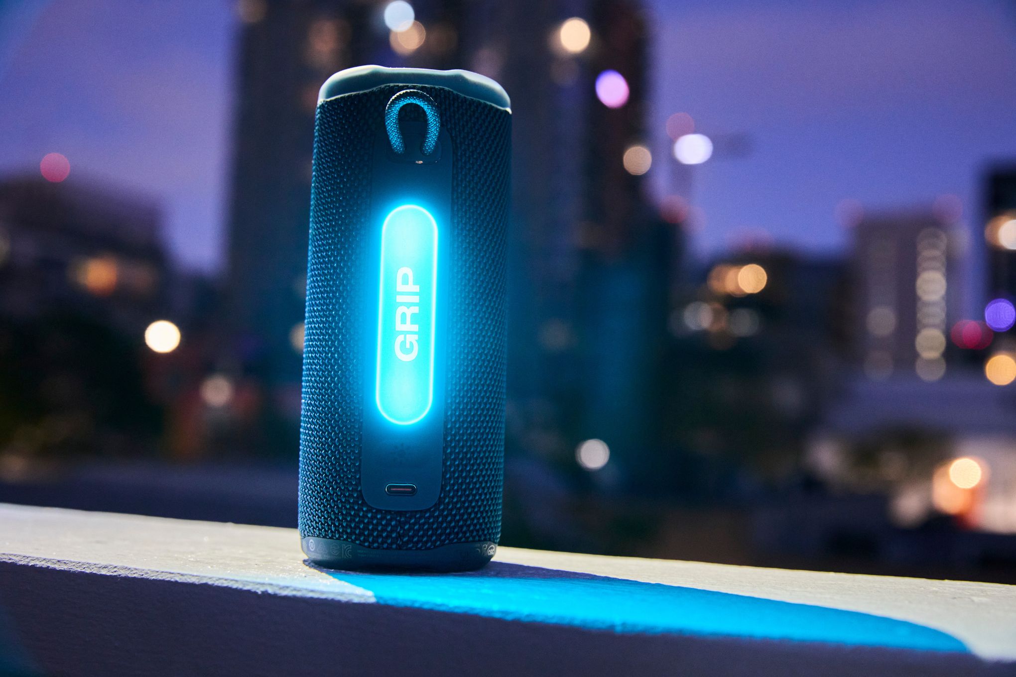 The JBL Grip Bluetooth speaker with a cityscape behind it.